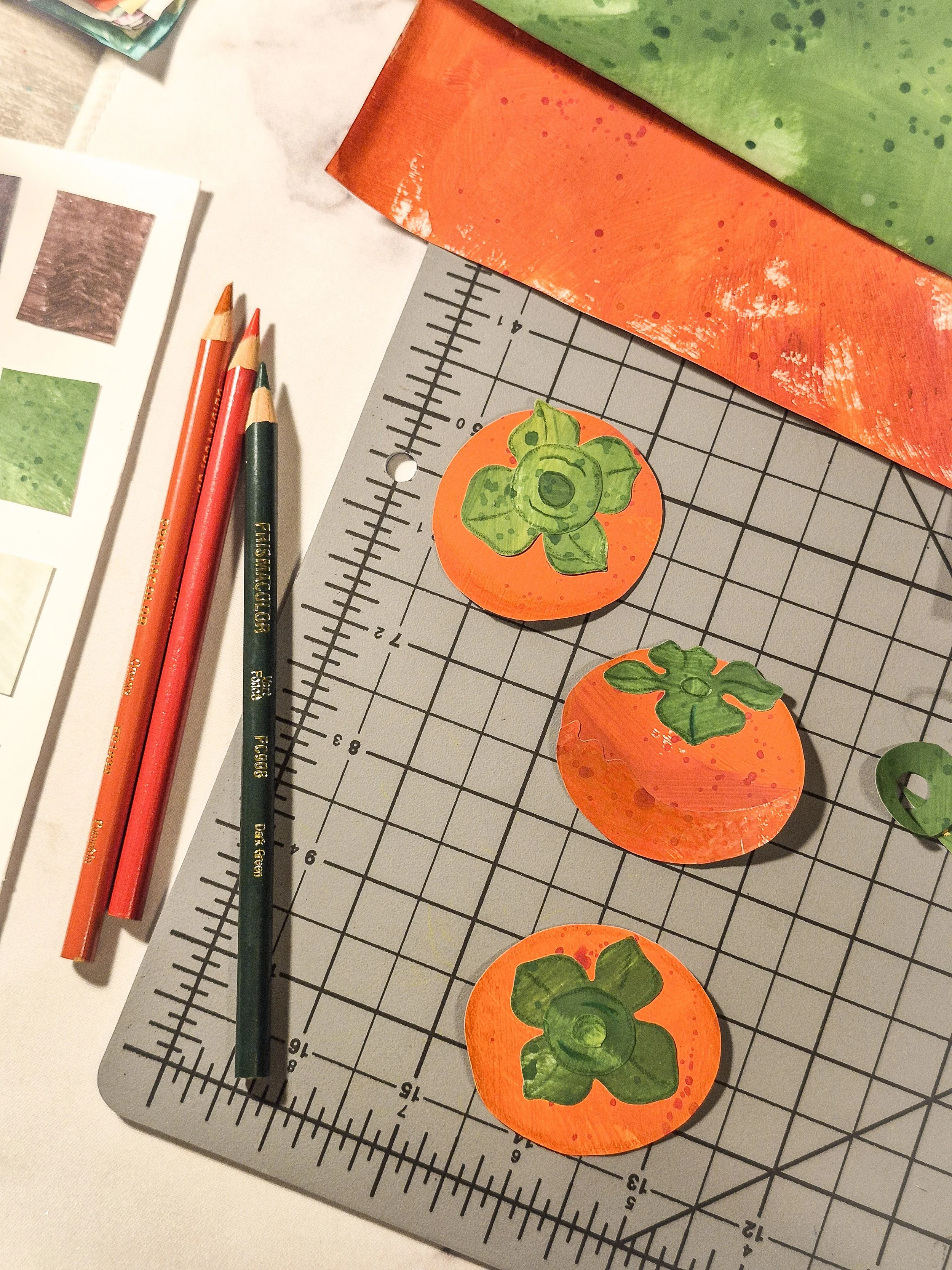 Hand-cut painted paper persimmon motifs with green leaves and painted paper scraps