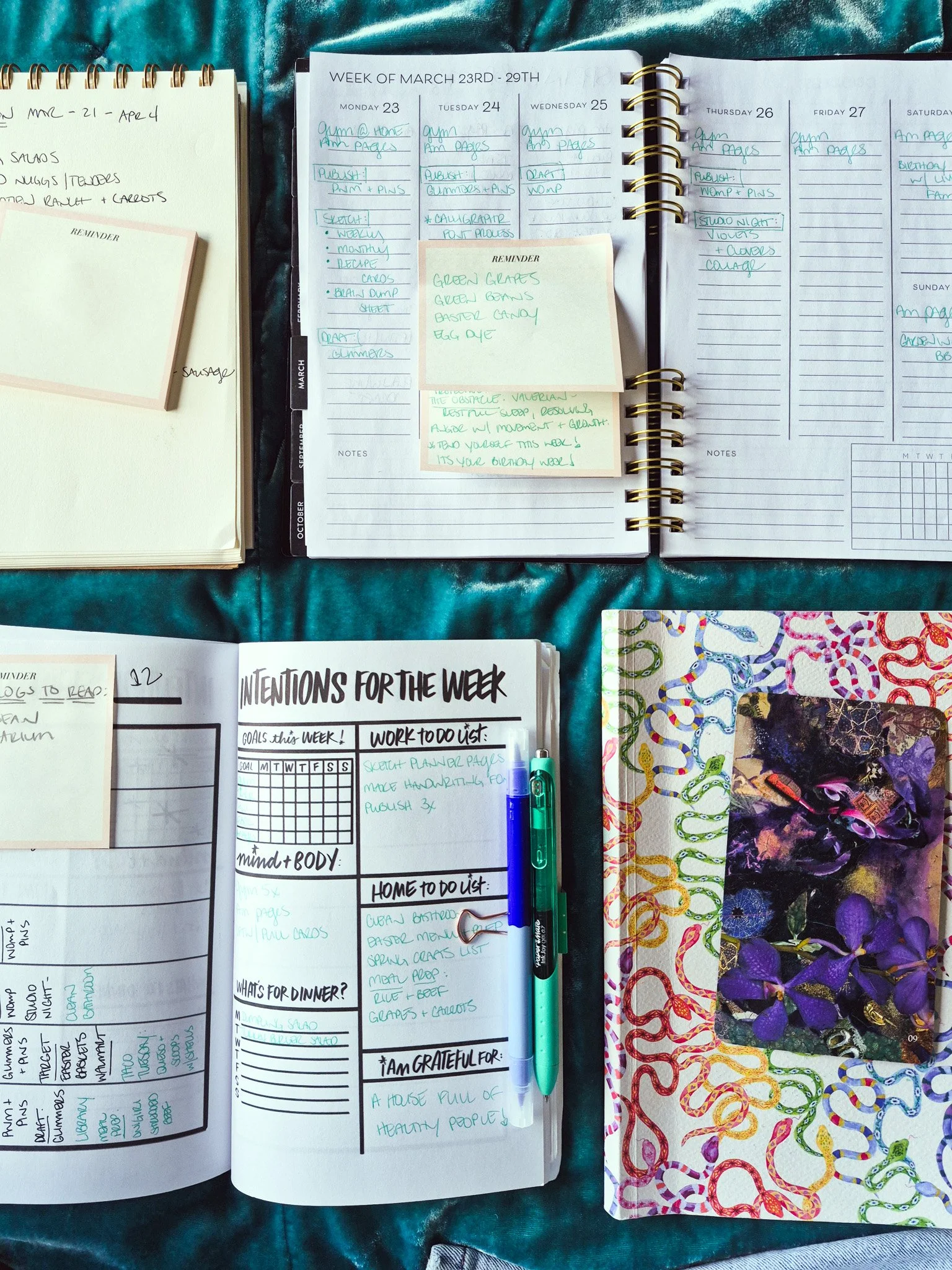 flat lay image of 2 open planners and spiral notebook and some pens on top of a teal velvet bed spread