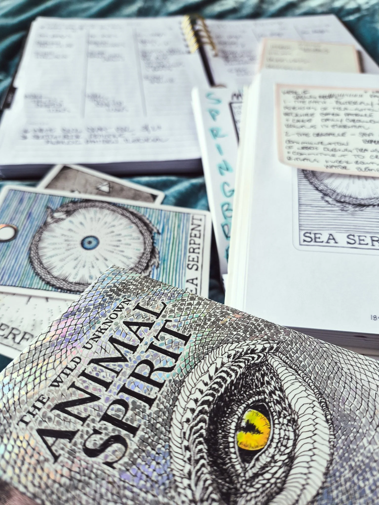 closeup of planners open on a teal velvet bedspread with two oracle cards from the wild unknown deck