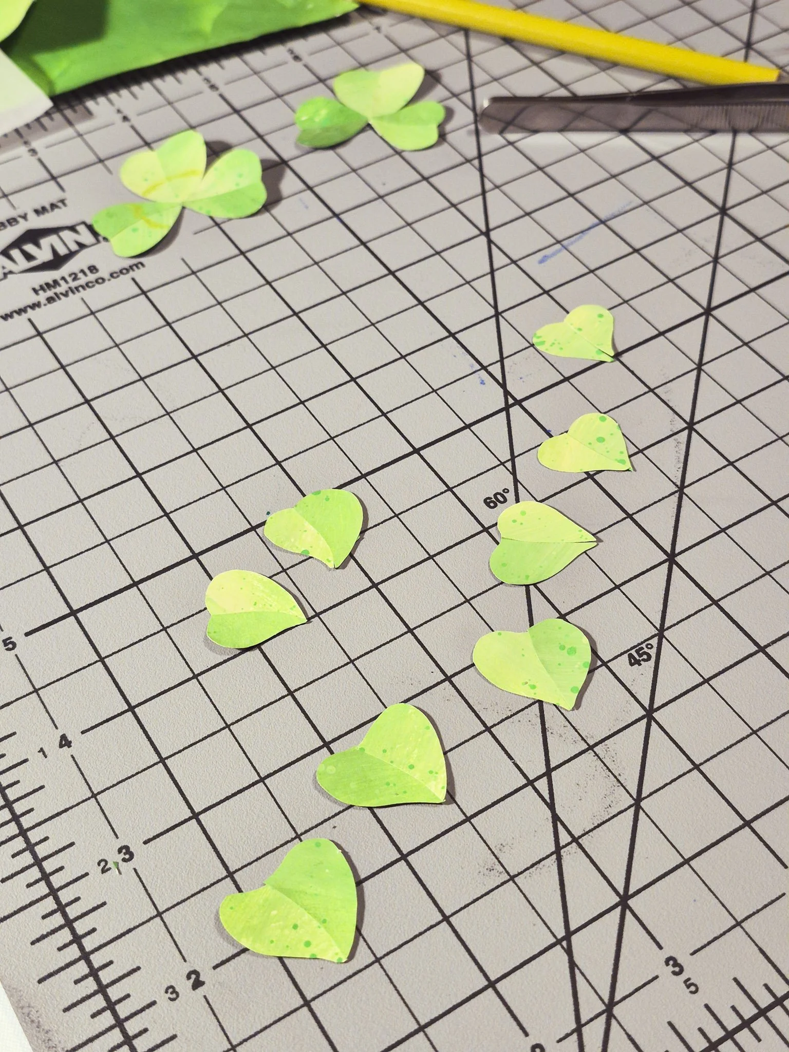 desk space image of painted paper clover leaves awaiting assembly on top of a grey cutting mat