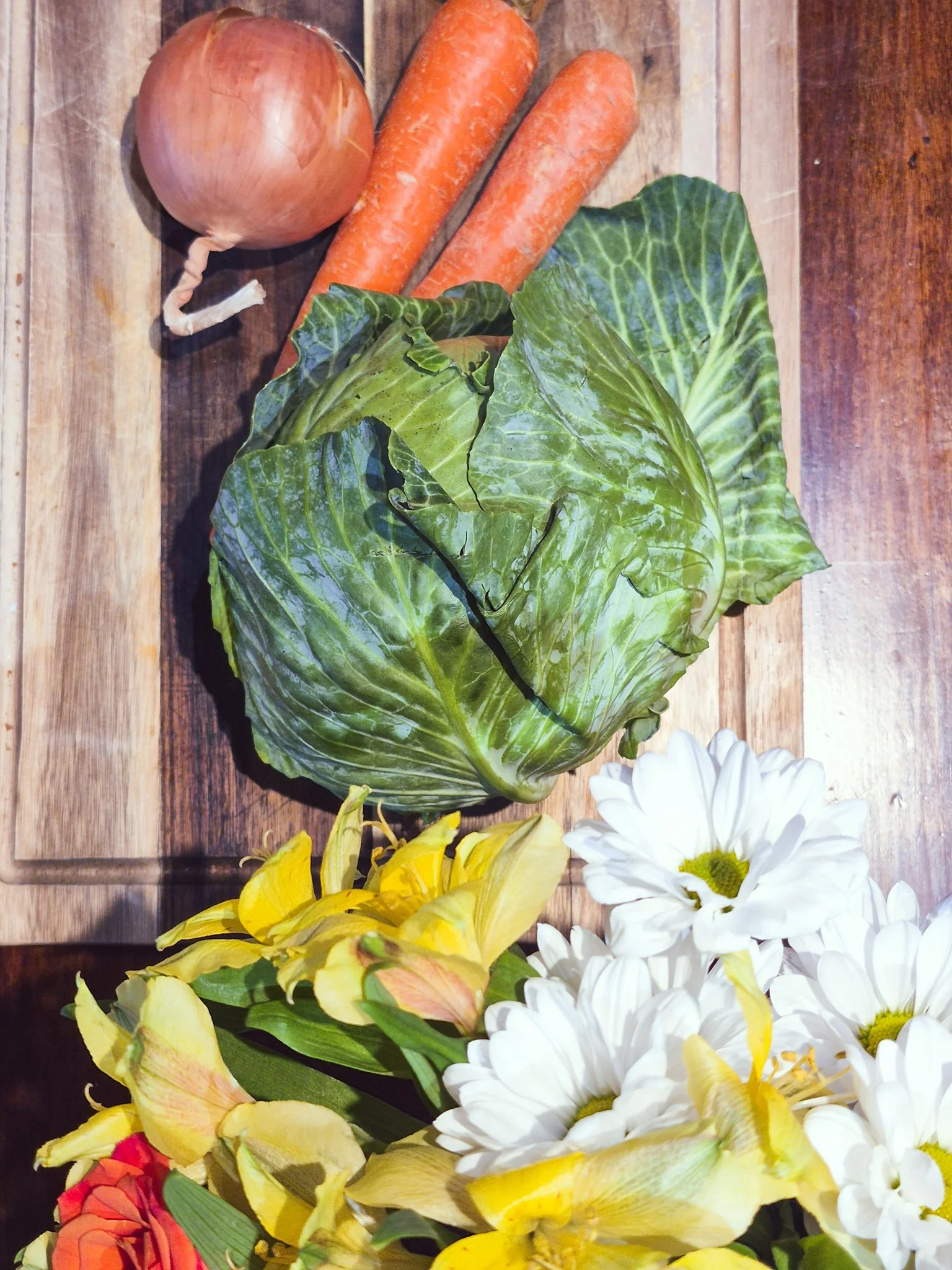 overhead image of a wooden cutting board with a grouping of cabbage carrots and onions before cutting