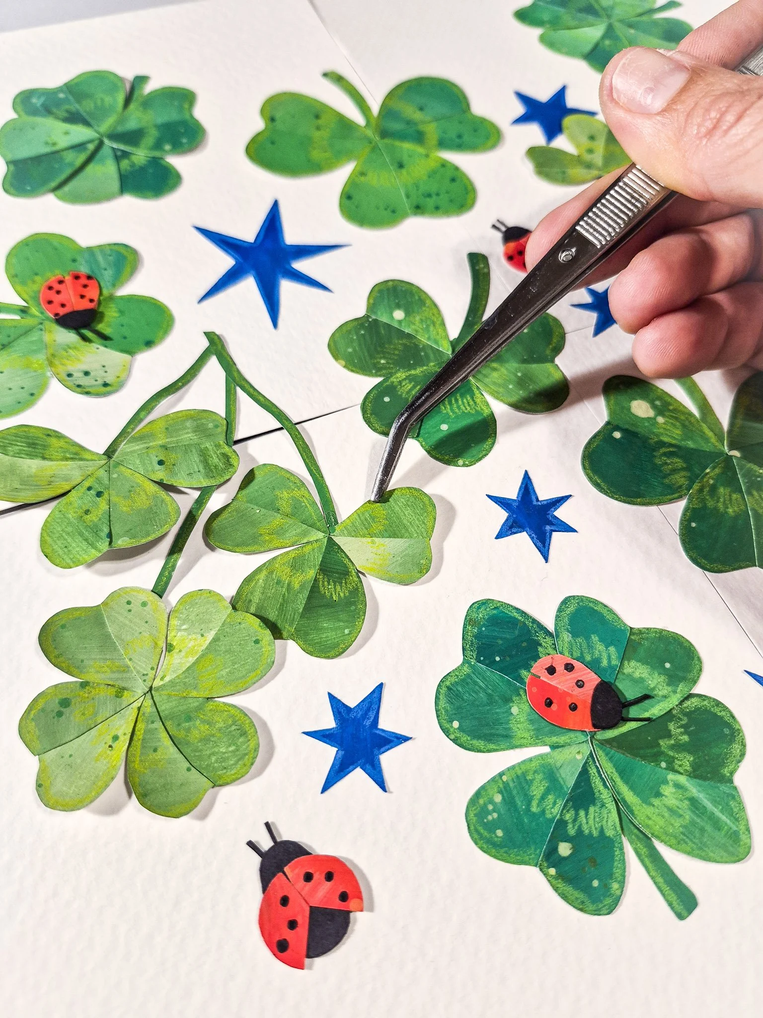 Using tweezers to carefully place collage elements while building an analog repeat pattern design