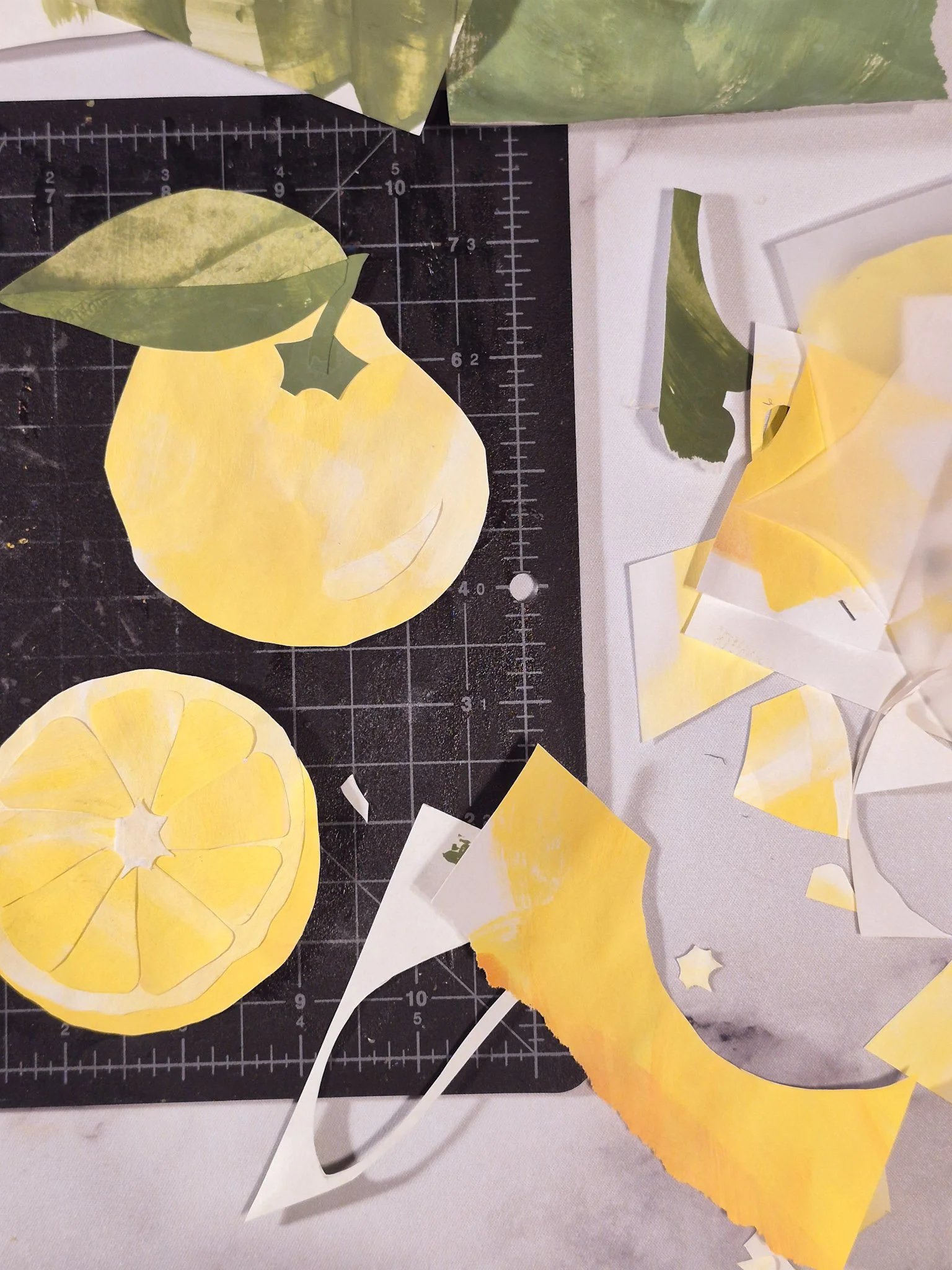 overhead desk photo with a painted paper collage yuzu fruit on a cutting mat with paper bits all around