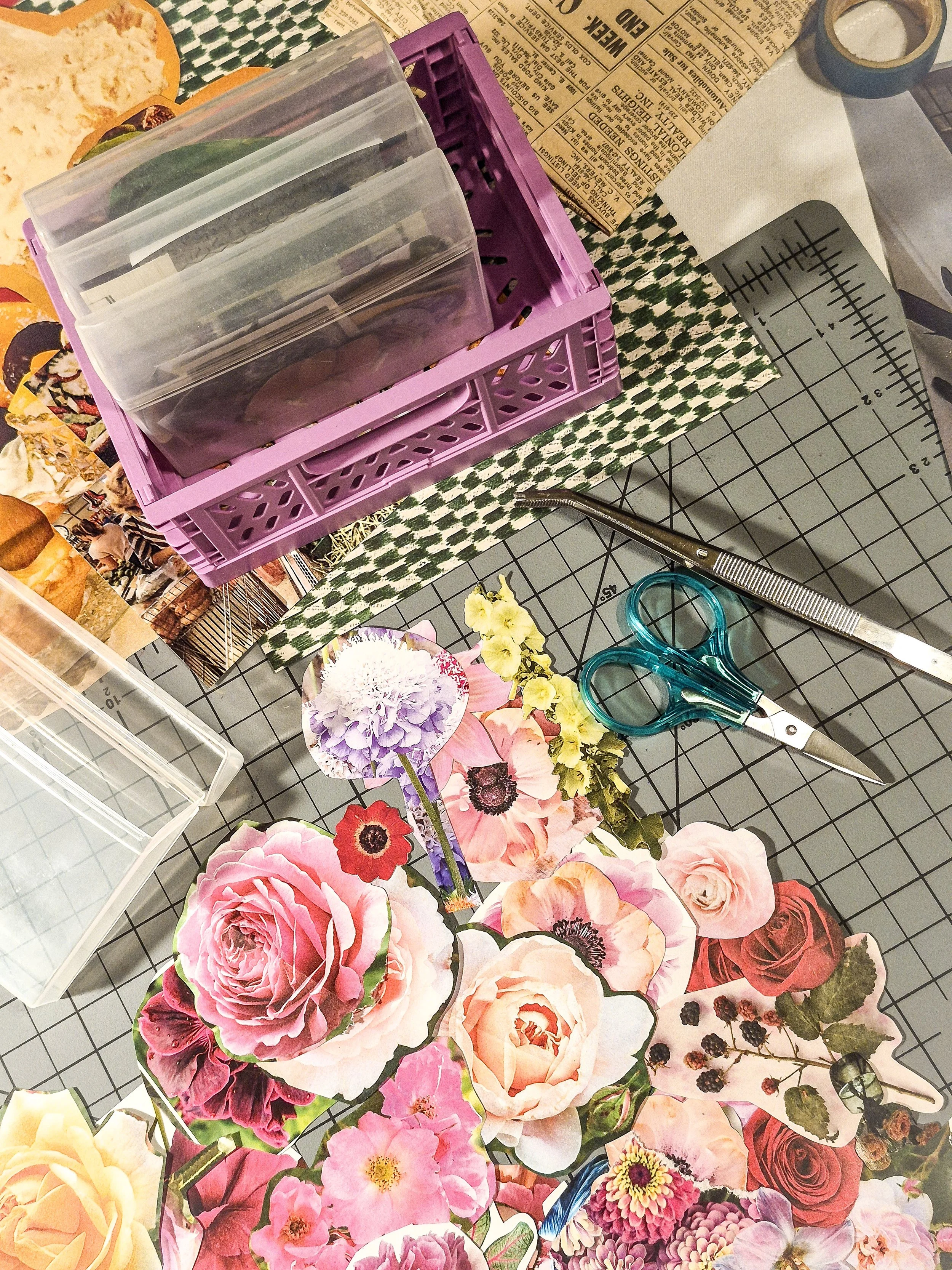 Cut-out vintage flowers and magazine imagery arranged on a cutting mat alongside collage papers, scissors, and a small storage box.