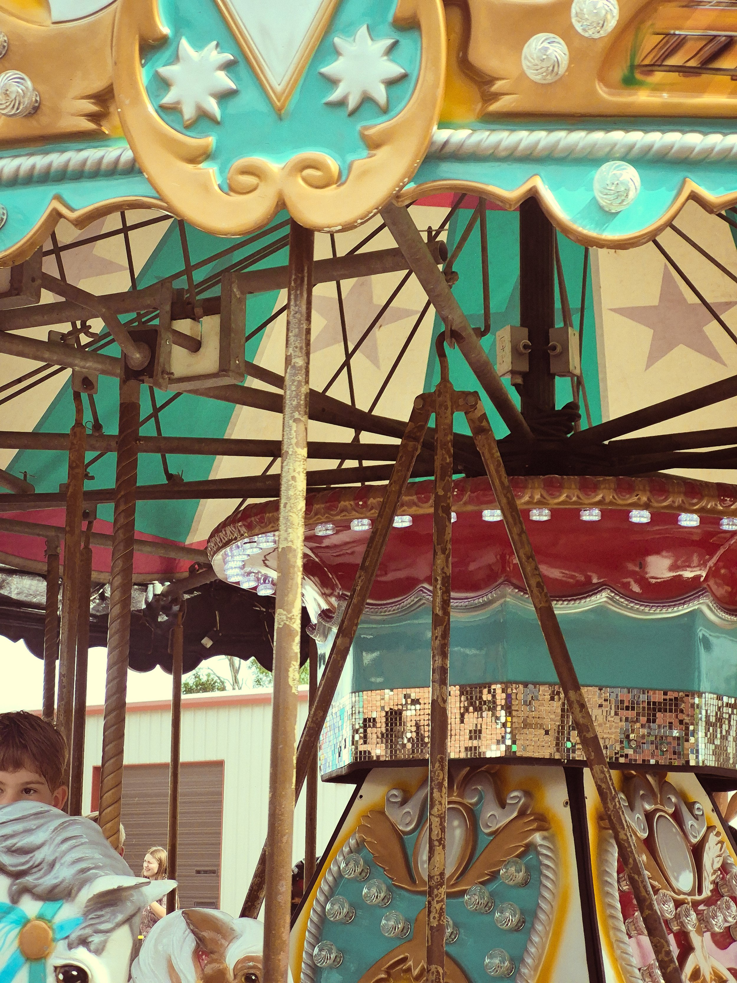 Close-up of a vintage carousel with turquoise, gold, pink, and red painted details and exposed metal framework.