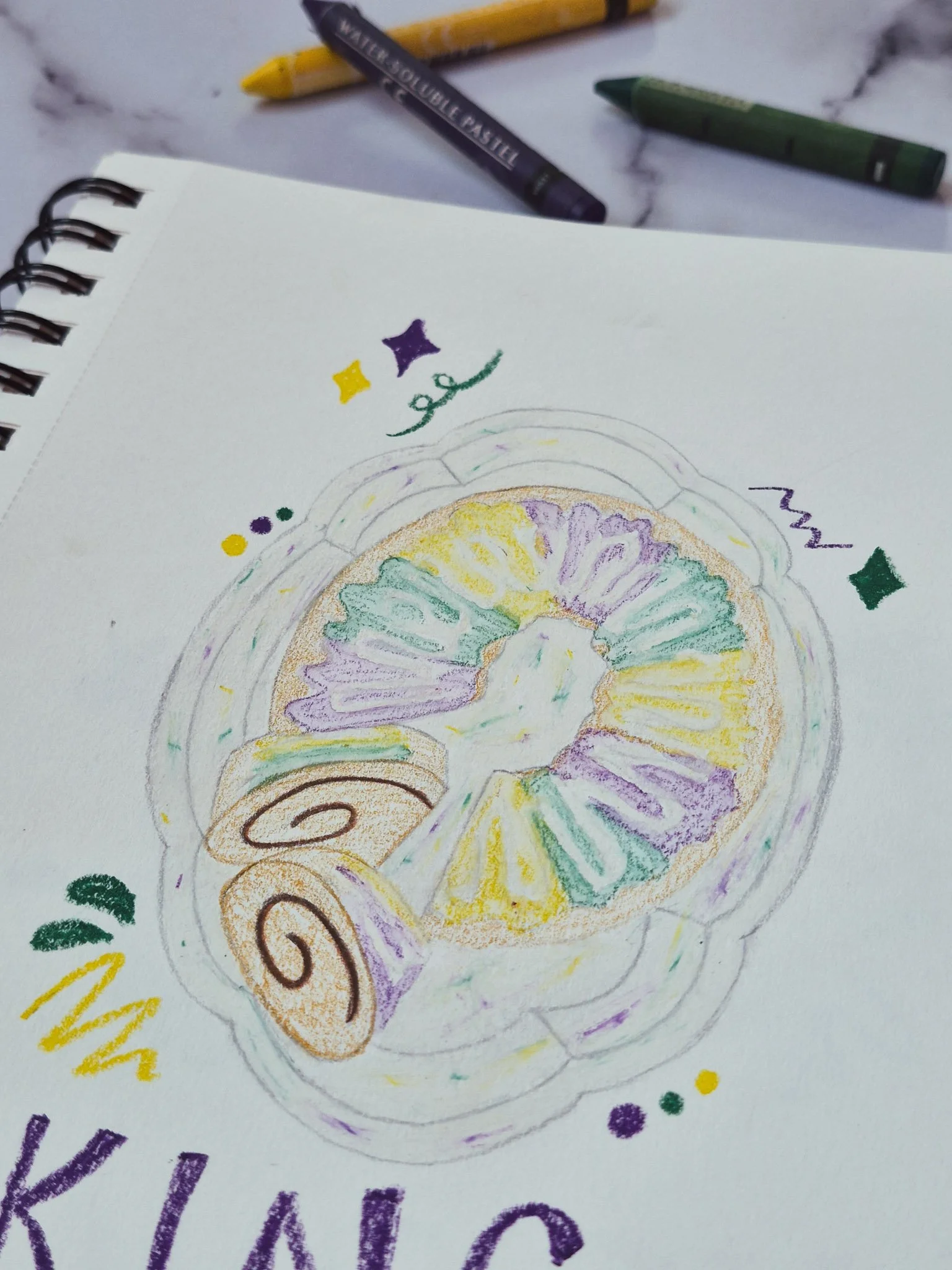 75 Art illustration of a king cake on a platter drawn in a sketchbook with water pastels nearby