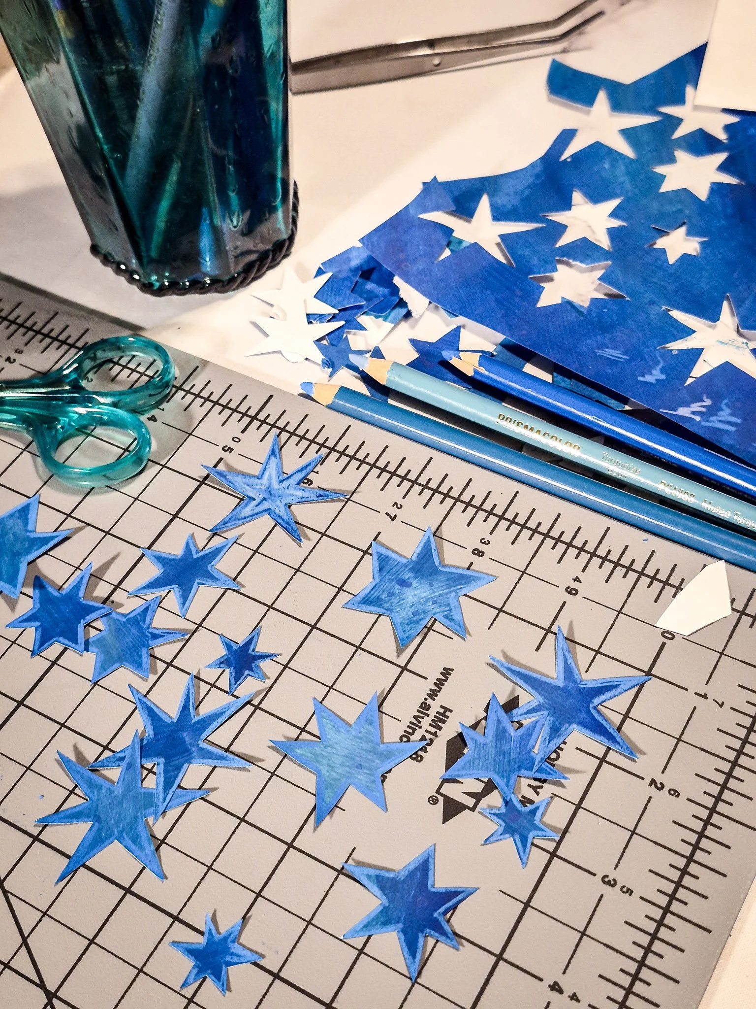 Blue hand-painted star paper cutouts scattered across a craft table with scissors and colored pencils.