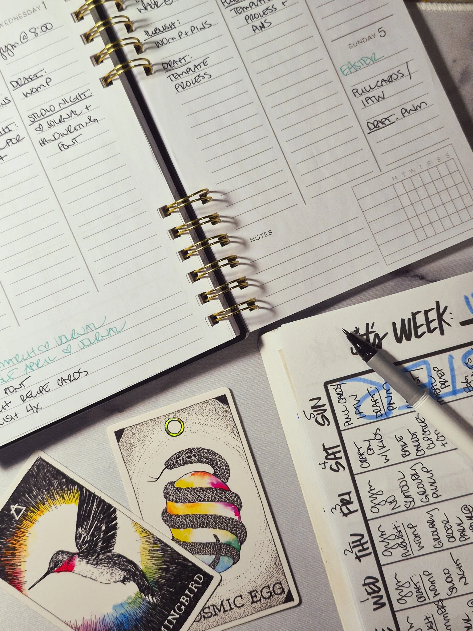 A cozy “plan with me” setup featuring an open weekly planner filled with handwritten notes, surrounded by soft lighting and neutral-toned stationery on a desk.