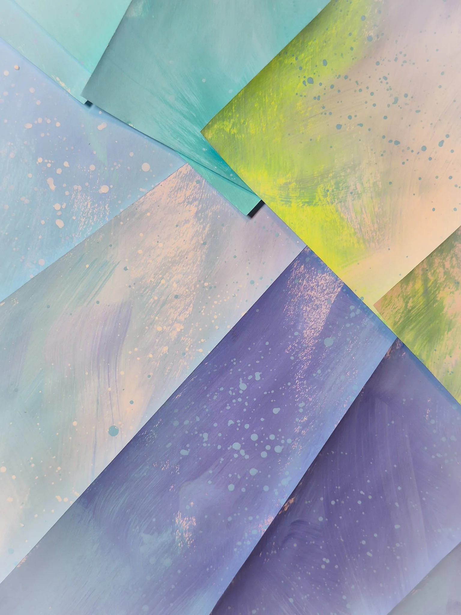 a pile of painted papers in a spring-hued palette of aquas, periwinkle, and a pop of neon yellow