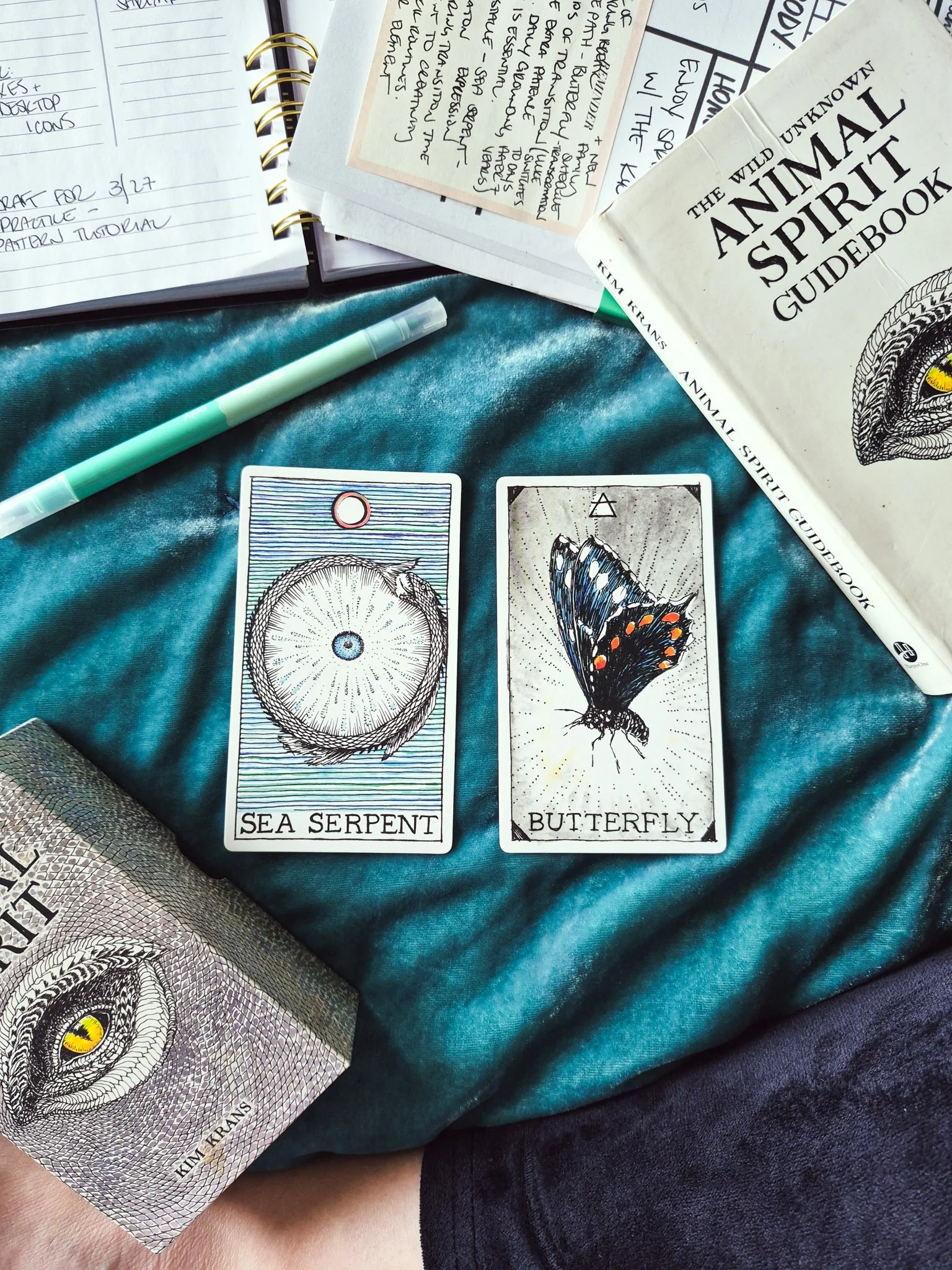 overhead image of two oracle cards framed by notepads and planners and guidebook