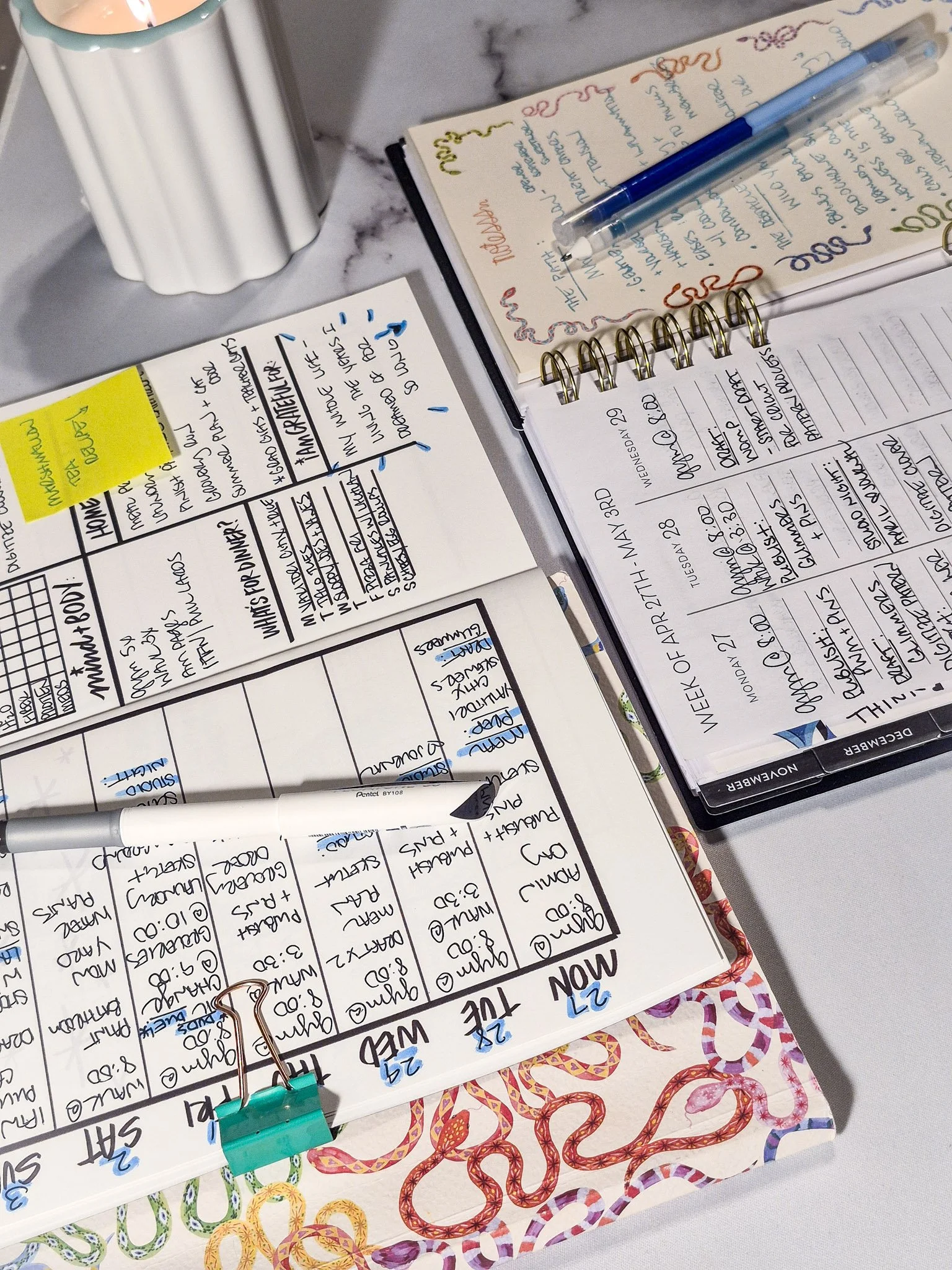 Cozy planning setup with open weekly planner, handwritten notes, patterned paper, and pens arranged on a marble desk