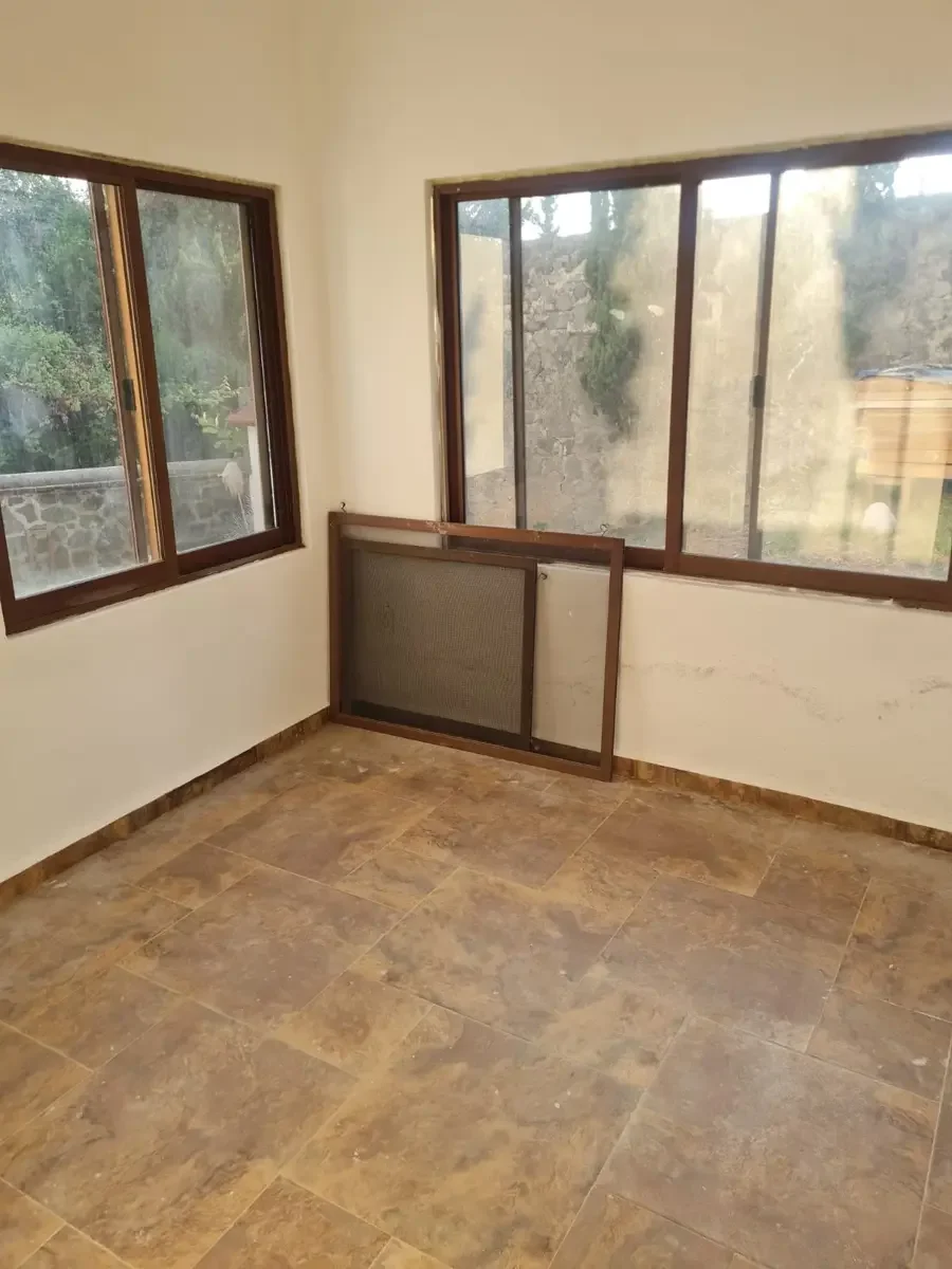 Cuatro ventanas de vidrio con marcos de madera y una malla de ventana en el suelo, en una habitación con paredes blancas y piso de cerámica beige.