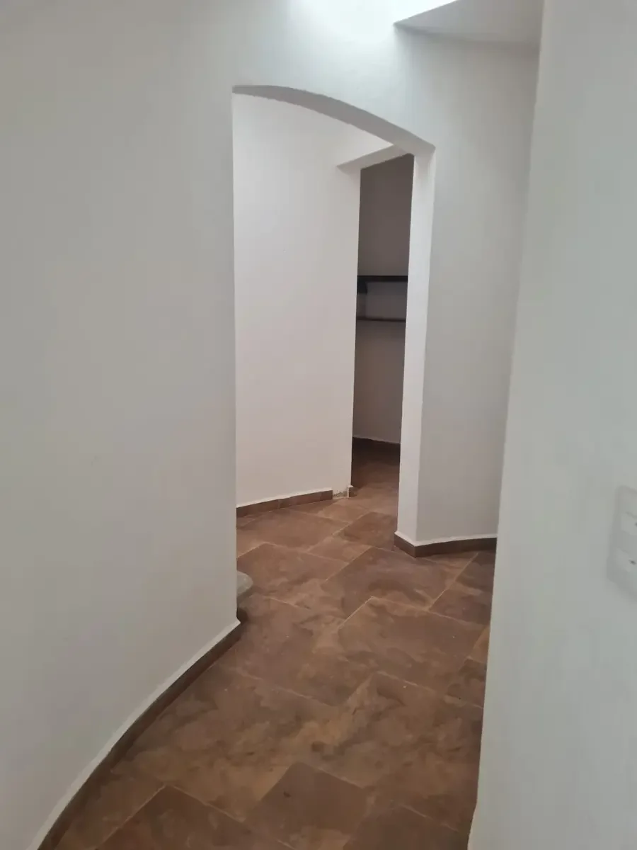 Pasillo con paredes blancas y piso de baldosas marrones, con entrada a un armario o almacenamiento.