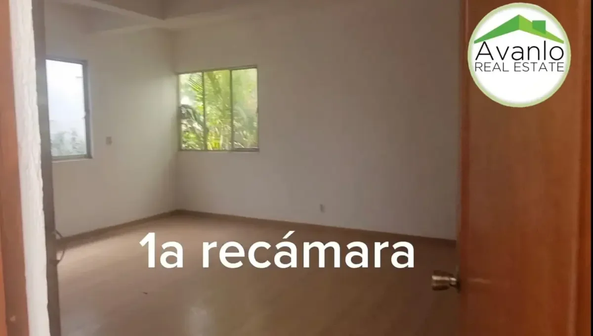Vista de una recámara vacía con ventanas y puertas de madera, paredes blancas y pisos de madera clara.