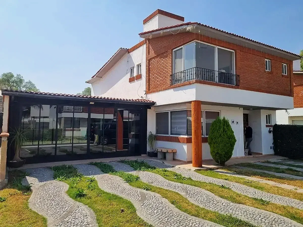 Casa moderna de dos pisos con paredes de ladrillo y ventanas grandes, rodeada de un jardín con senderos de piedra y césped.