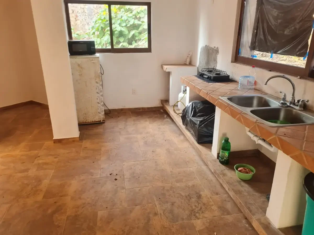 Cocina en construcción o en reparación, con un fregadero doble, estufa de gas, ventana y algunos objetos de cocina dispersos.