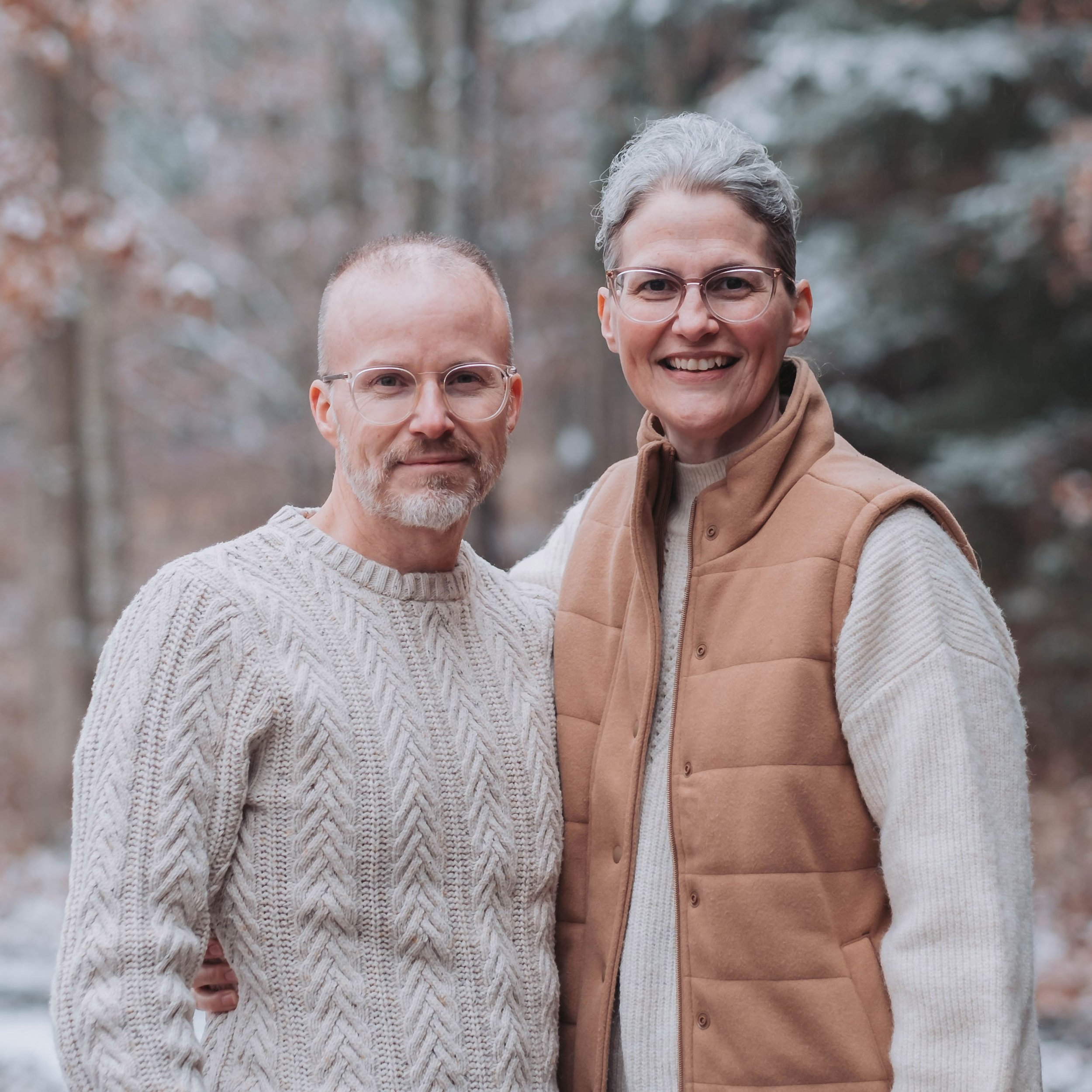 Pastor Brad and Heidi Carpenter standing outdoors in a winter setting with blurred bare trees in the background, smiling and close together.