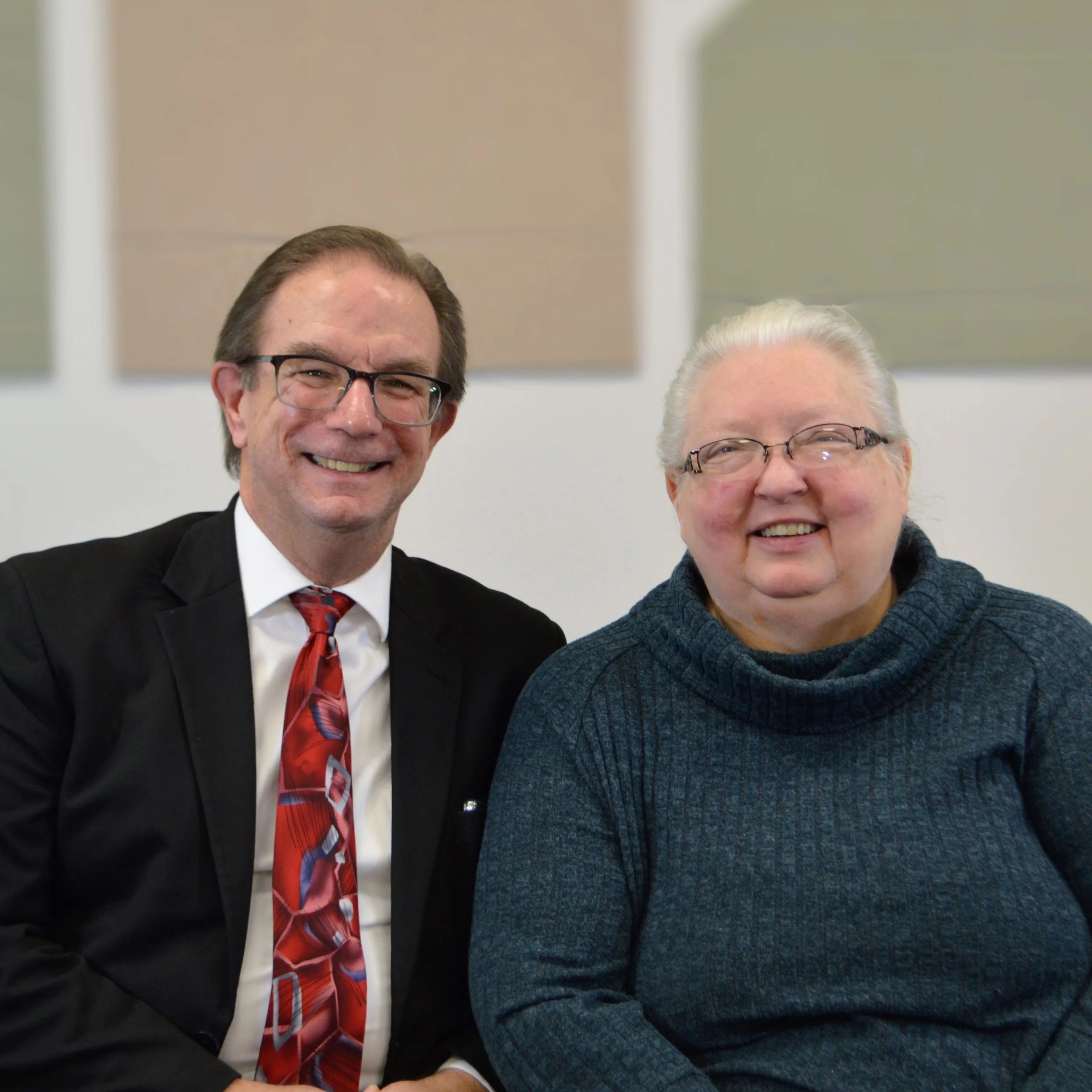 A portrait of Bishop Ed and Mina Nichols, both smiling at the camera. Background features an abstract beige and greenish artwork.