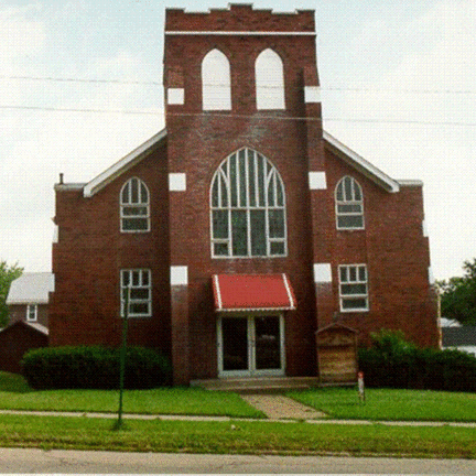 A historic brick church with a tall tower, arched windows, and a red awning at the entrance.