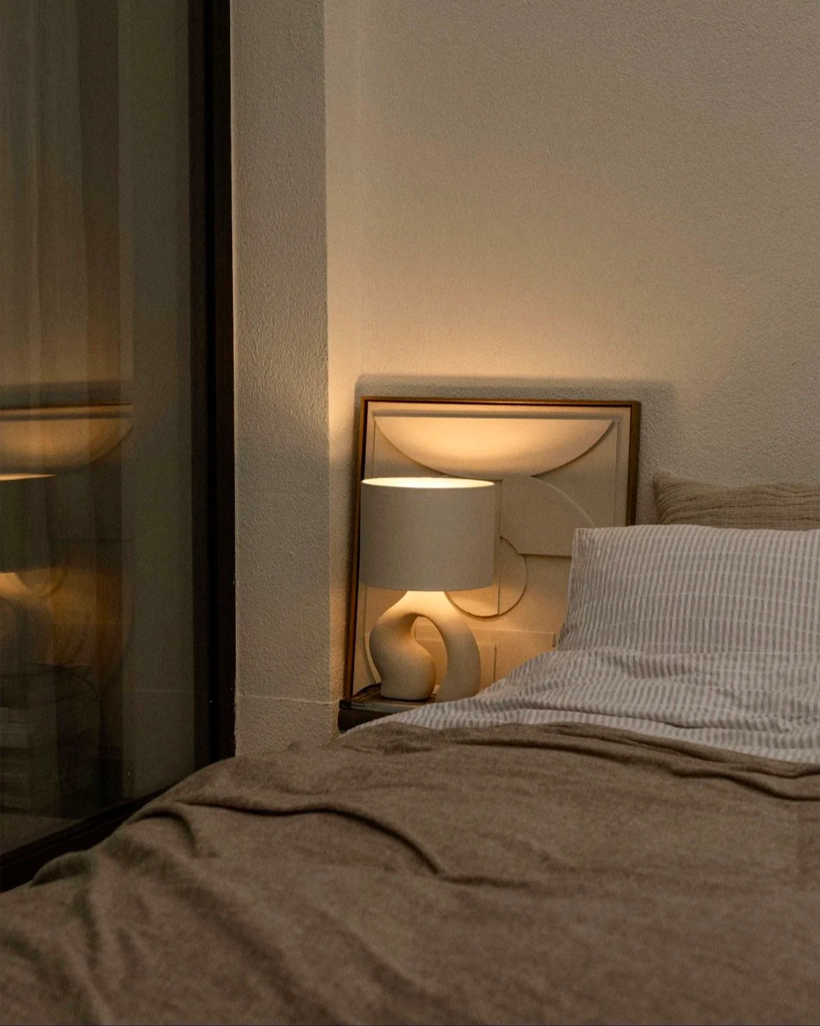 lamp lit beside a bed in the evening