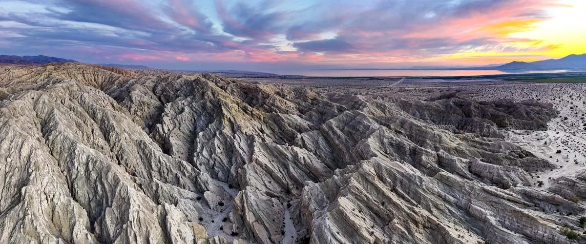 A landscape of rugged, layered hills and mountains during sunset with a colorful sky of purple, pink, orange, and yellow hues at Chuckwalla National Monument