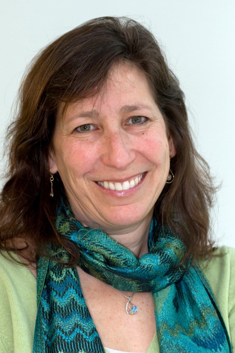 Karen Harris with brown hair smiling, wearing earrings, a necklace, and a blue-green patterned scarf.