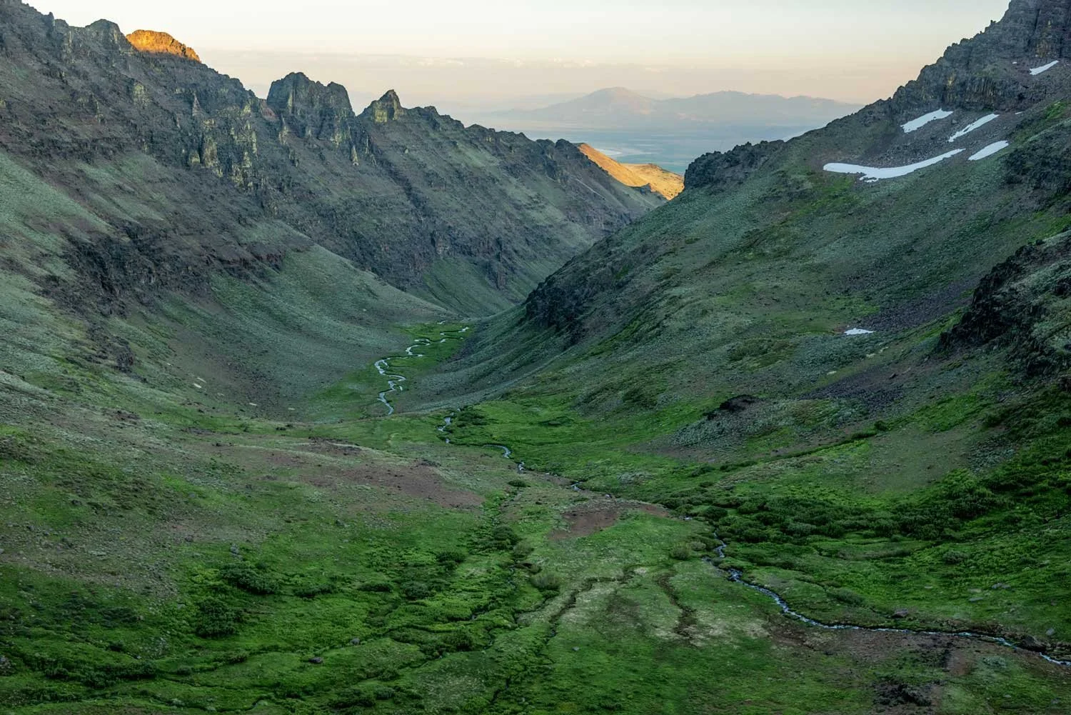 valley between mountain ranges covered in low vegetation with water winding through