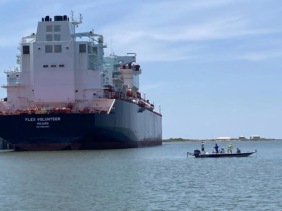 large cargo ship sitting in a channel with a fishing boat nearby with a handful of people on it.