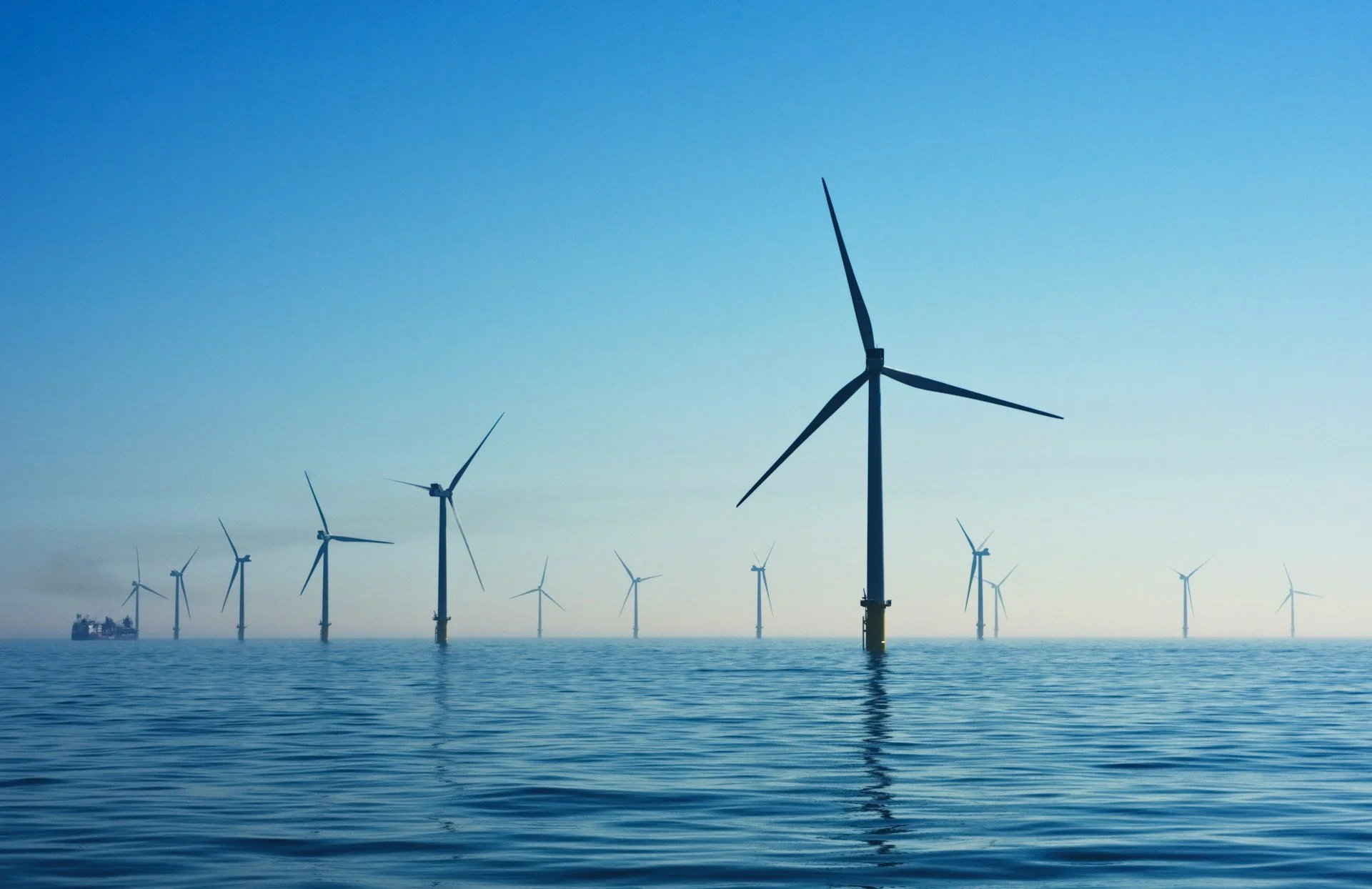 Offshore wind turbines standing in the ocean under a clear blue sky.