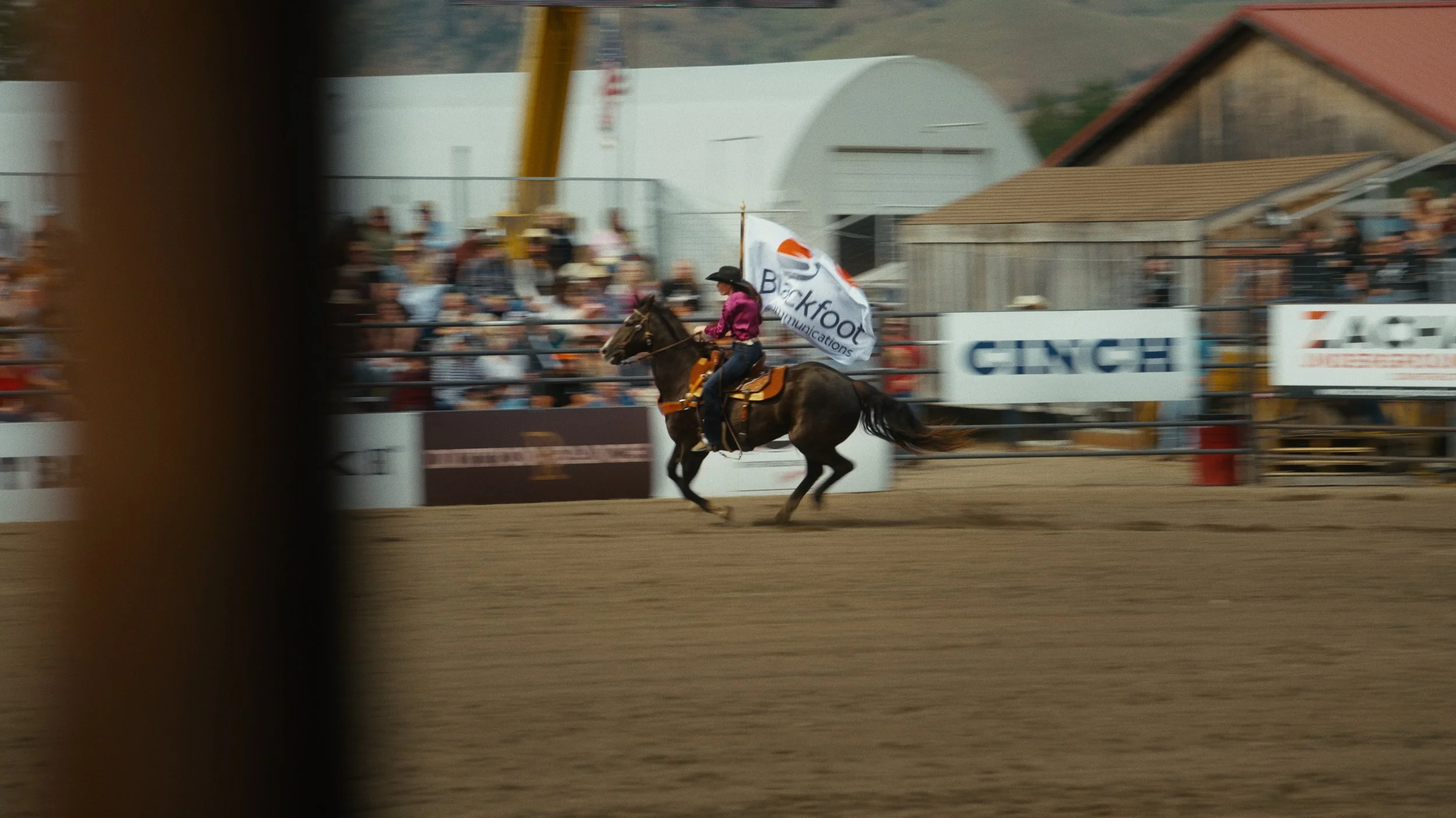 Rider on horseback holding a flag during a rodeo event with spectators in the background.