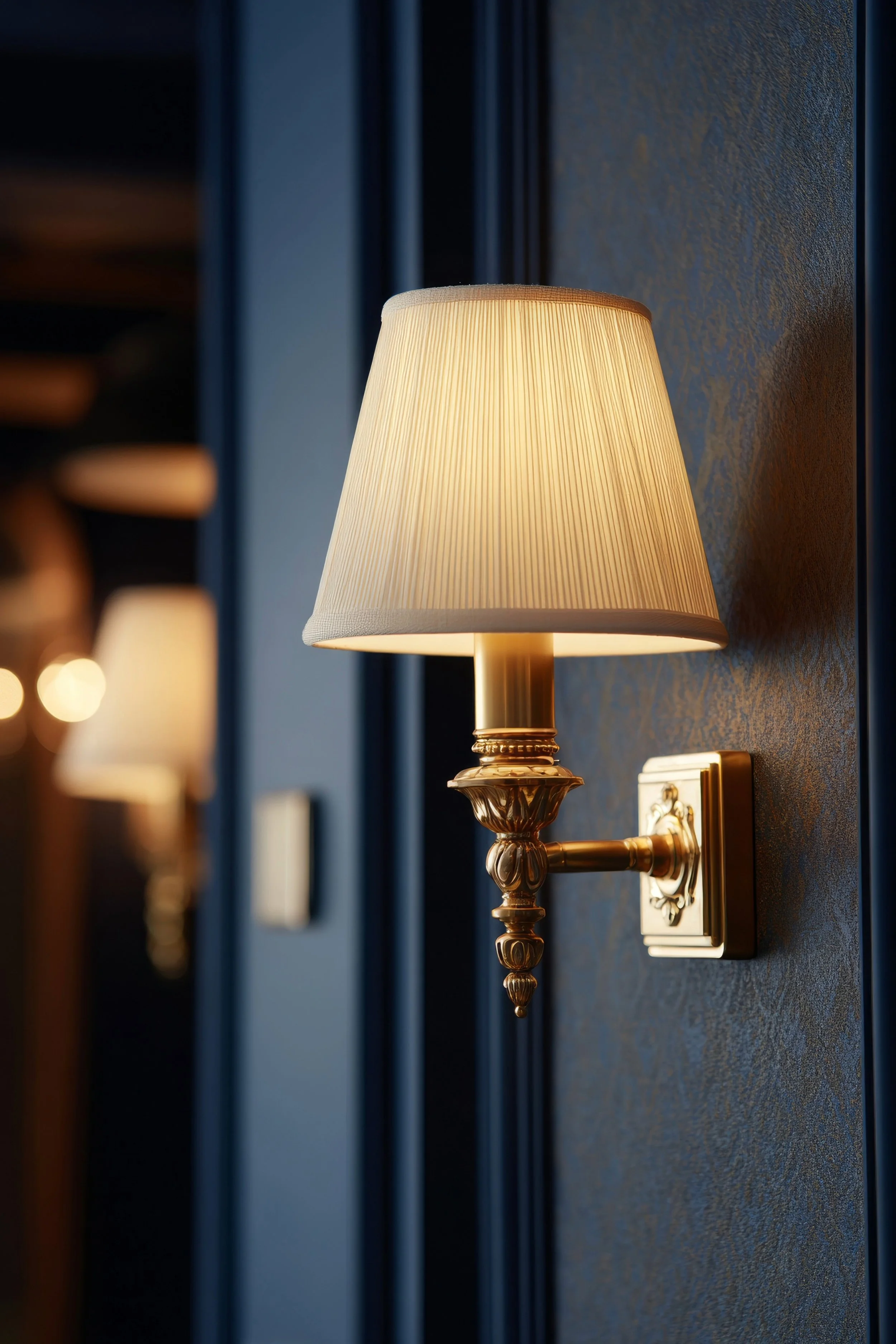 Brass wall lamp with white shade glows softly on living room wall, warm night light in classic style.