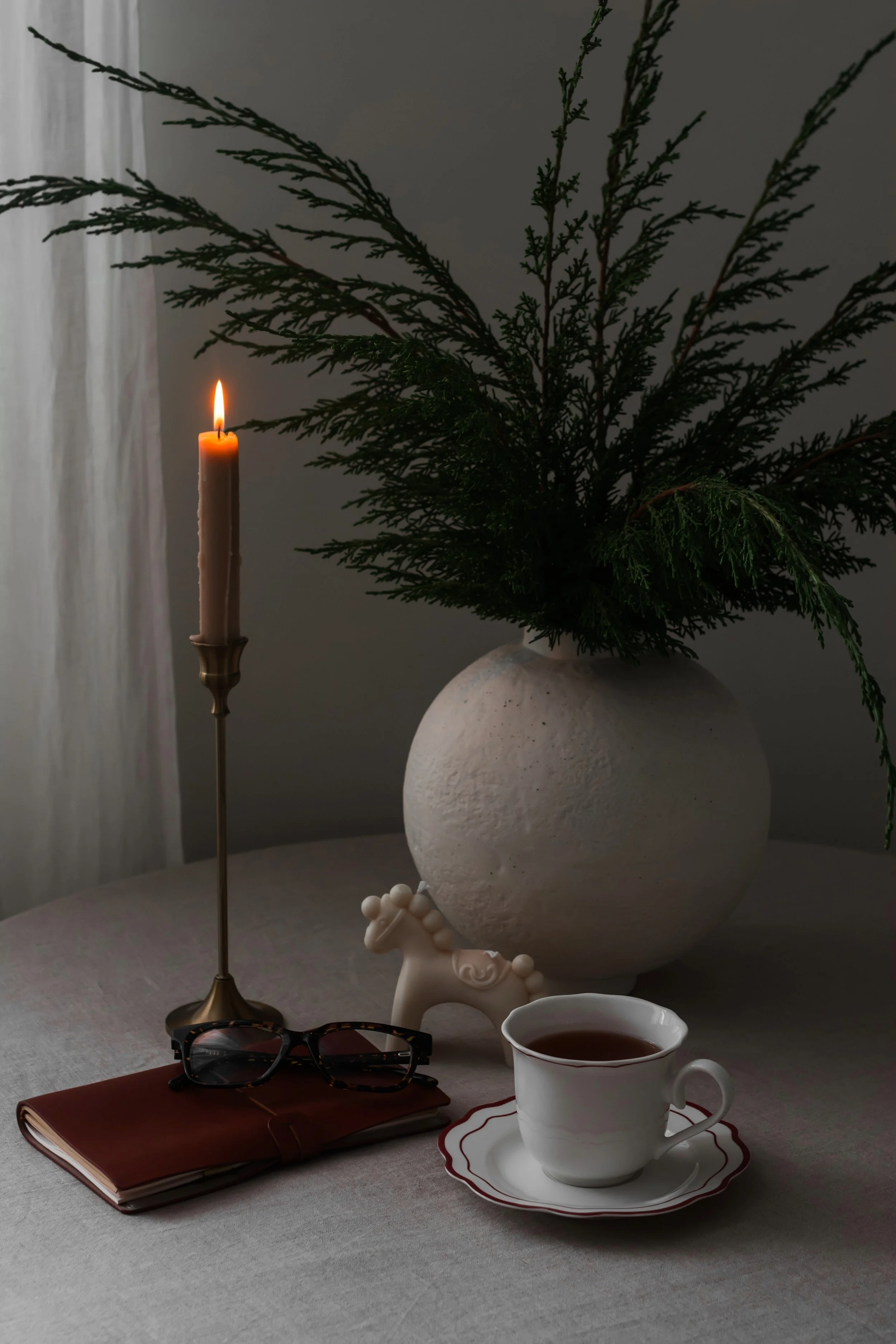 A cup of coffee, a candle in a brass holder, a bouquet in a ceramic vase on a table with a gray tablecloth