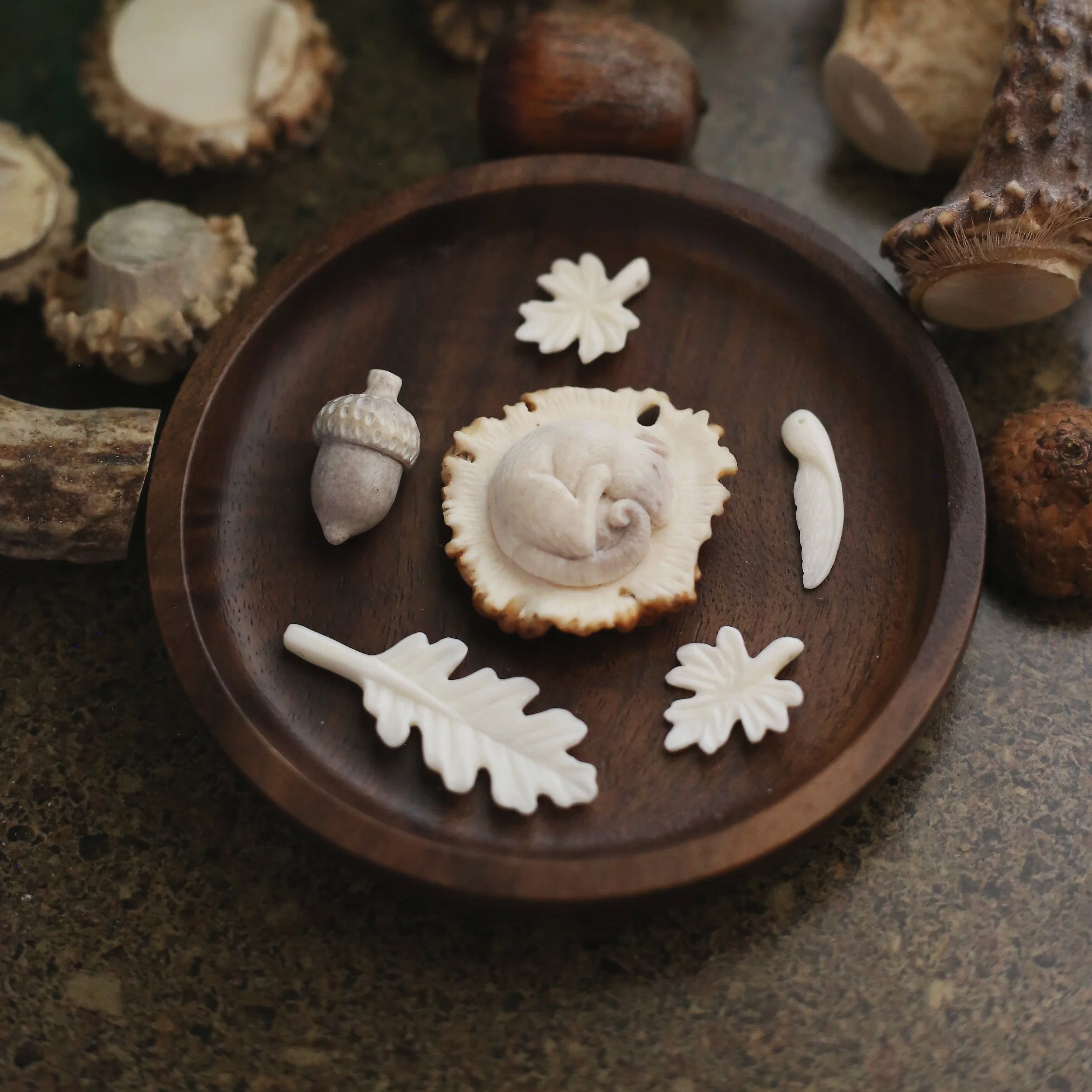 A collection of carvings made from bone and antler. Door mouse on antler root, leaves made from bone, acorn from antler. 