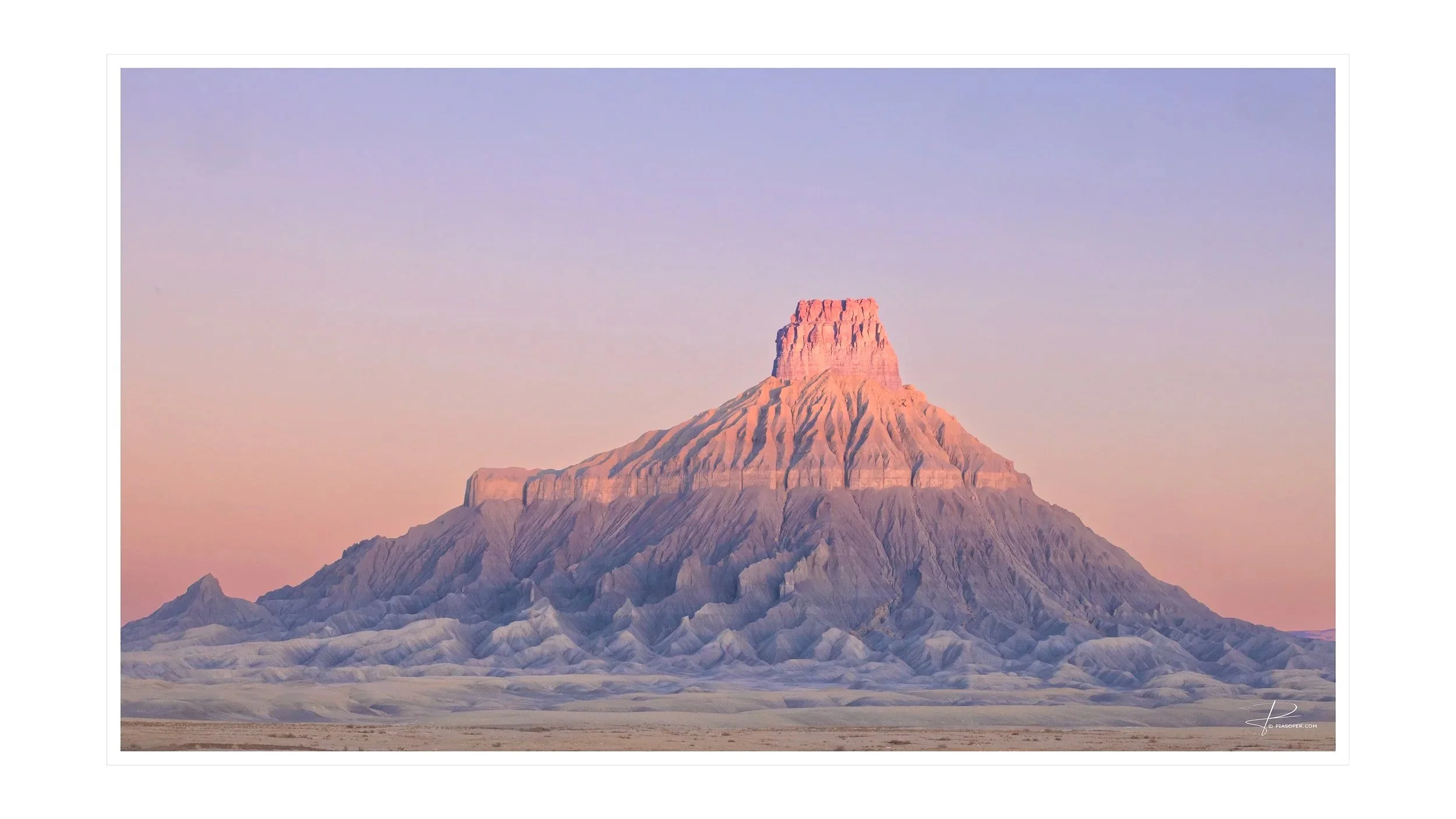 Factory Butte, Capitol Reef National Park Utah.  New Dawn with pastel colors of the butte from base to top being whites blues violets and pinks. Sun rising on the butte top. Sky is orange to pink to yellow to viotets and blue as go higher