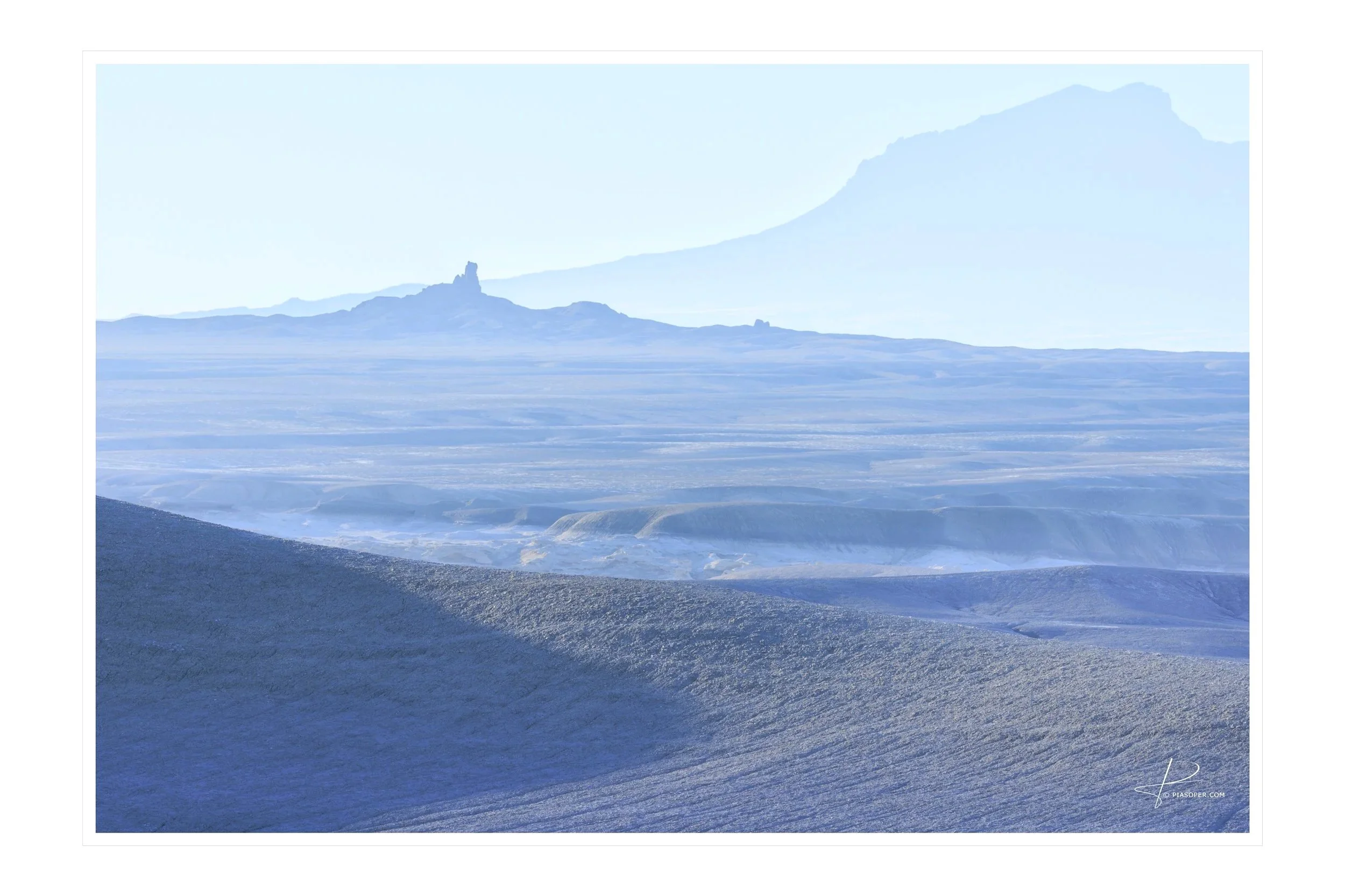 Layers of blue in a Southern Utah desert sunrise. Canyons of mud  and spires in the distance along with a tall mountain range. Taken near Factory Butte in Capitol Reef National Park. Copyright Pia Soper 2026 all rights reserved