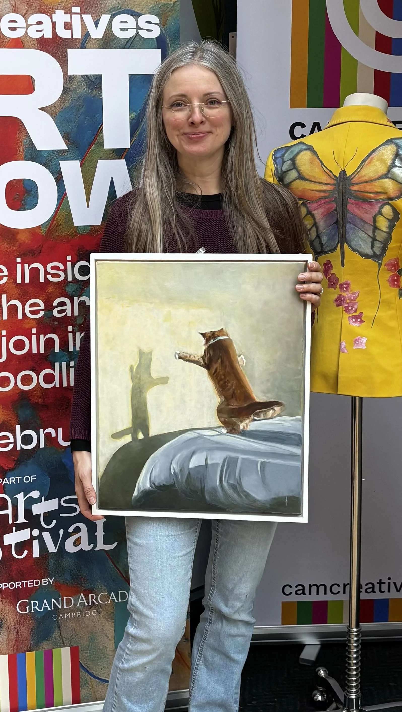 Artist, Monica Alikoviene, holding the framed oil painting Golden Hour at the Cam Creatives art event in Cambridge.