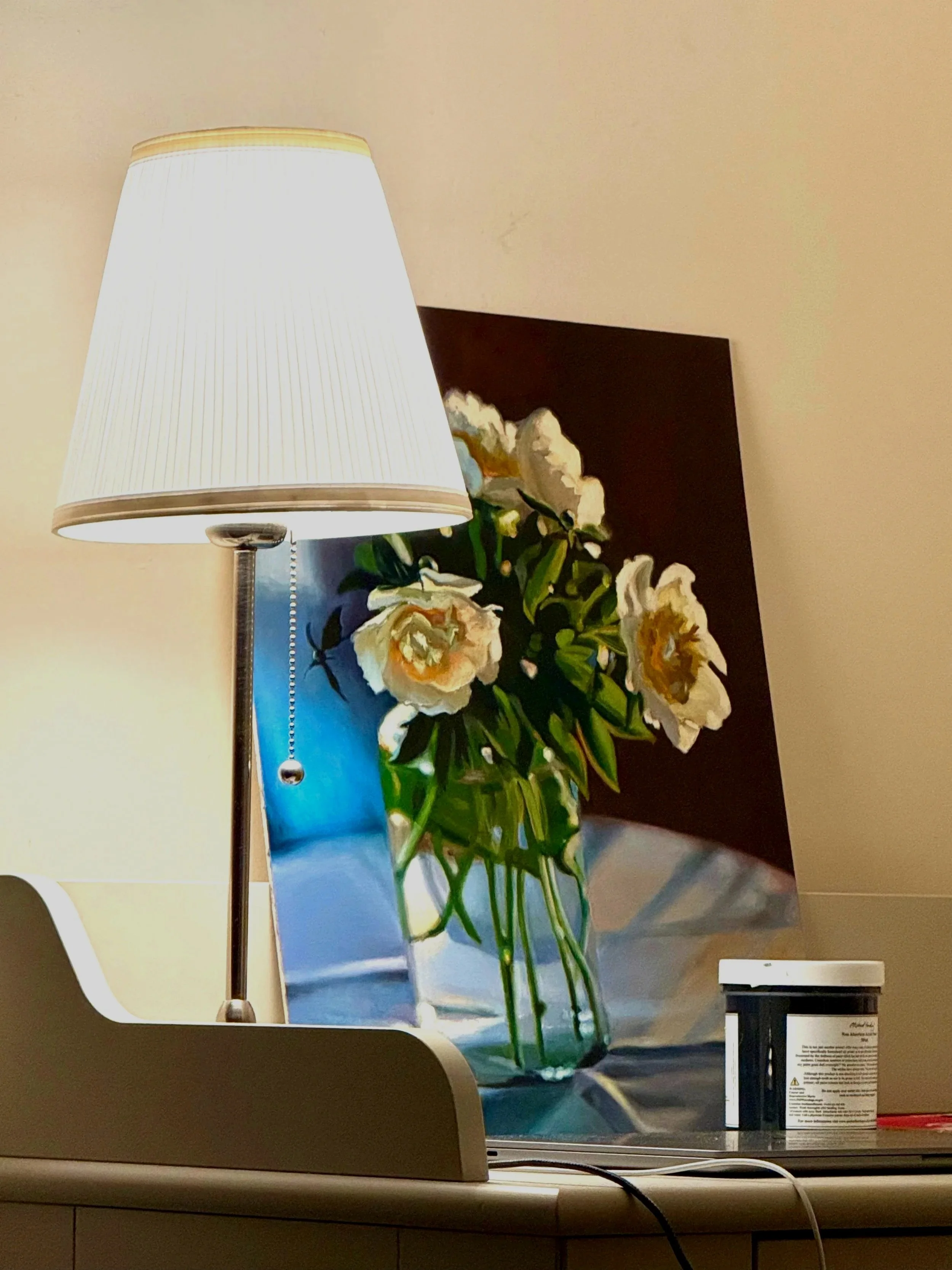 A computer screen displaying a photo of a white flower arrangement on a black background, with a white desk lamp positioned on the left side of the screen.