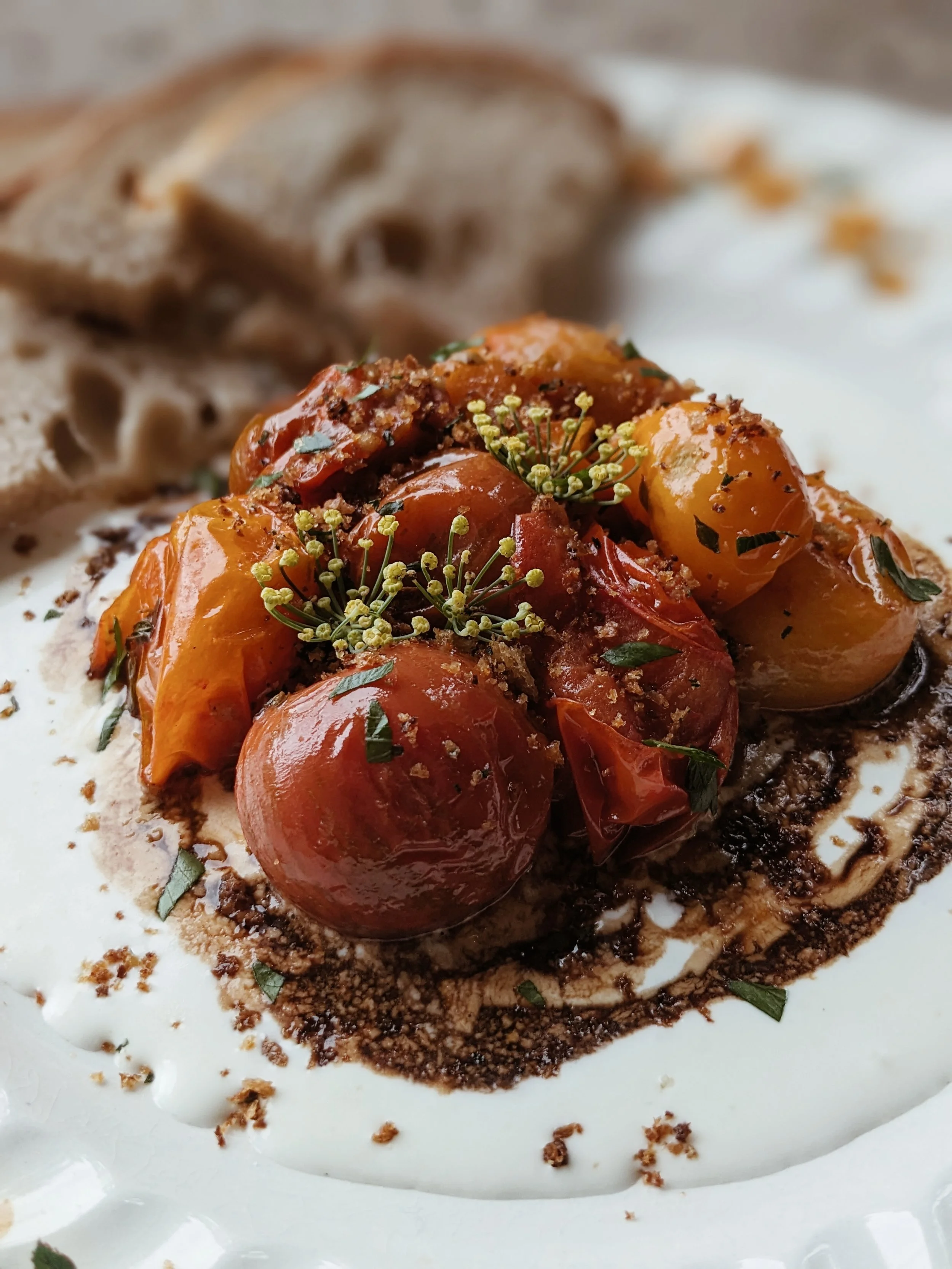 Plate with roasted cherry tomatoes, garnished with herbs, served with slices of sliced bread