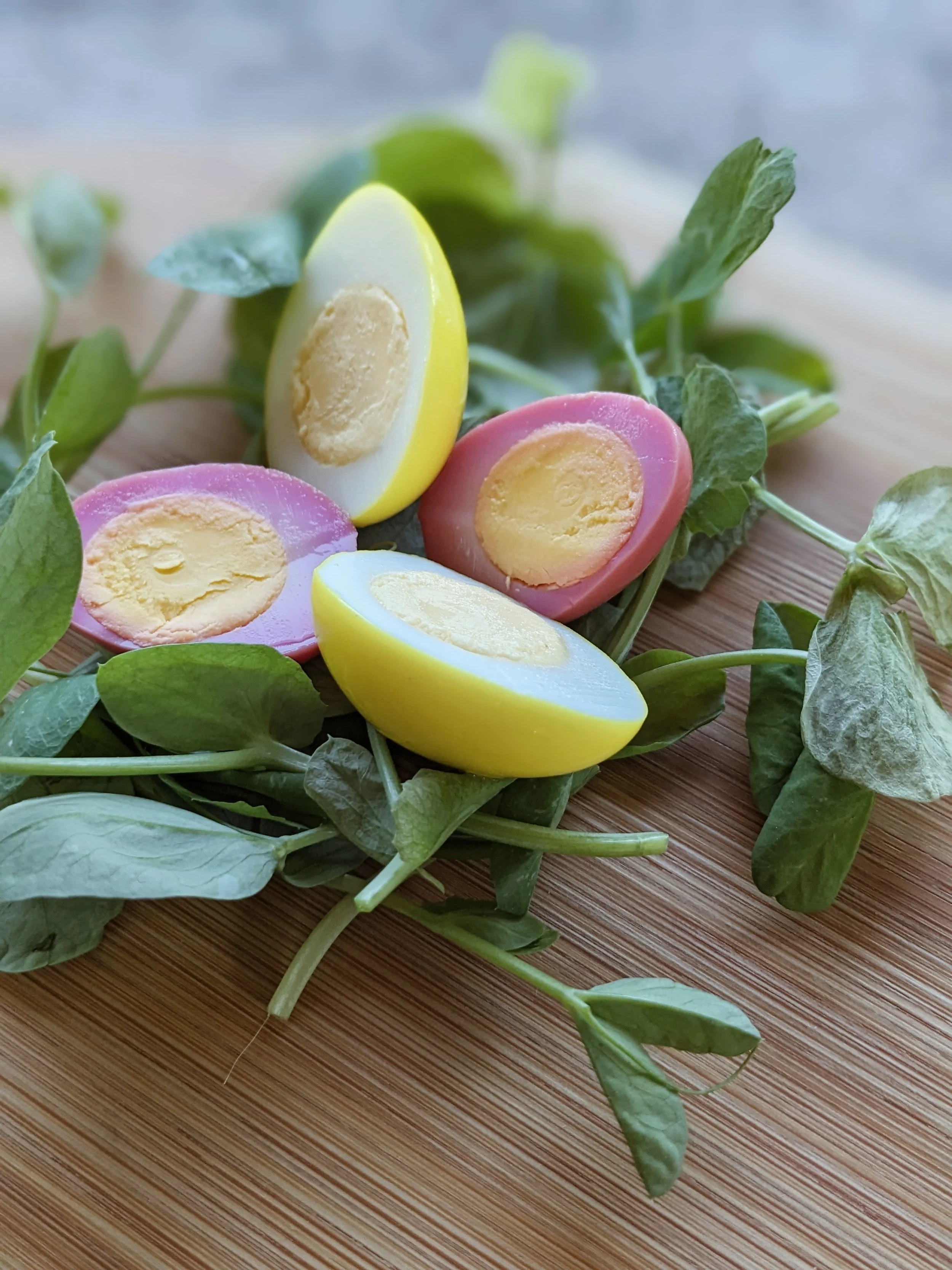 Colorful boiled eggs on a wooden surface surrounded by leafy greens.