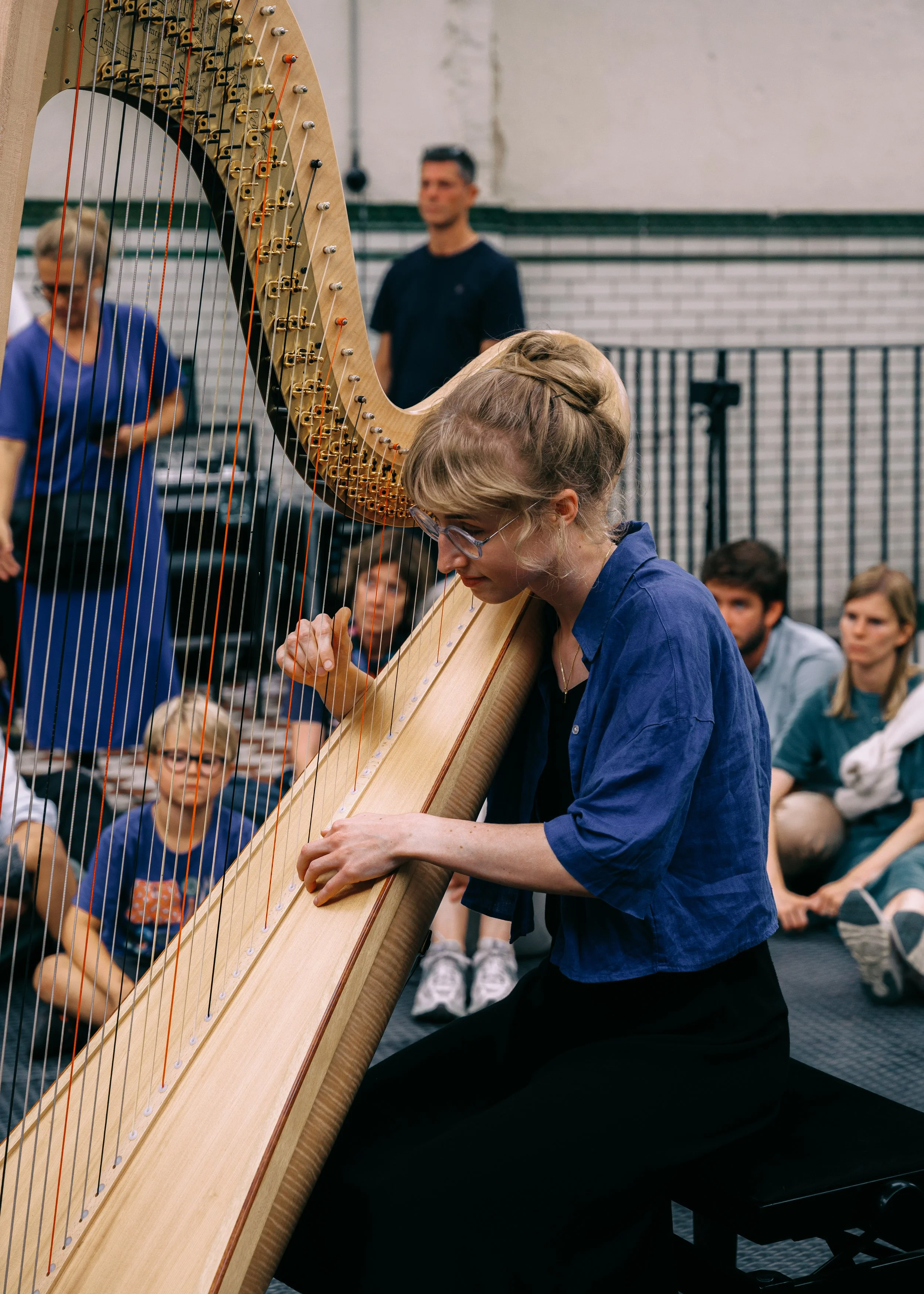 A woman playing a harp while surrounded by children and adults in a music workshop or class.