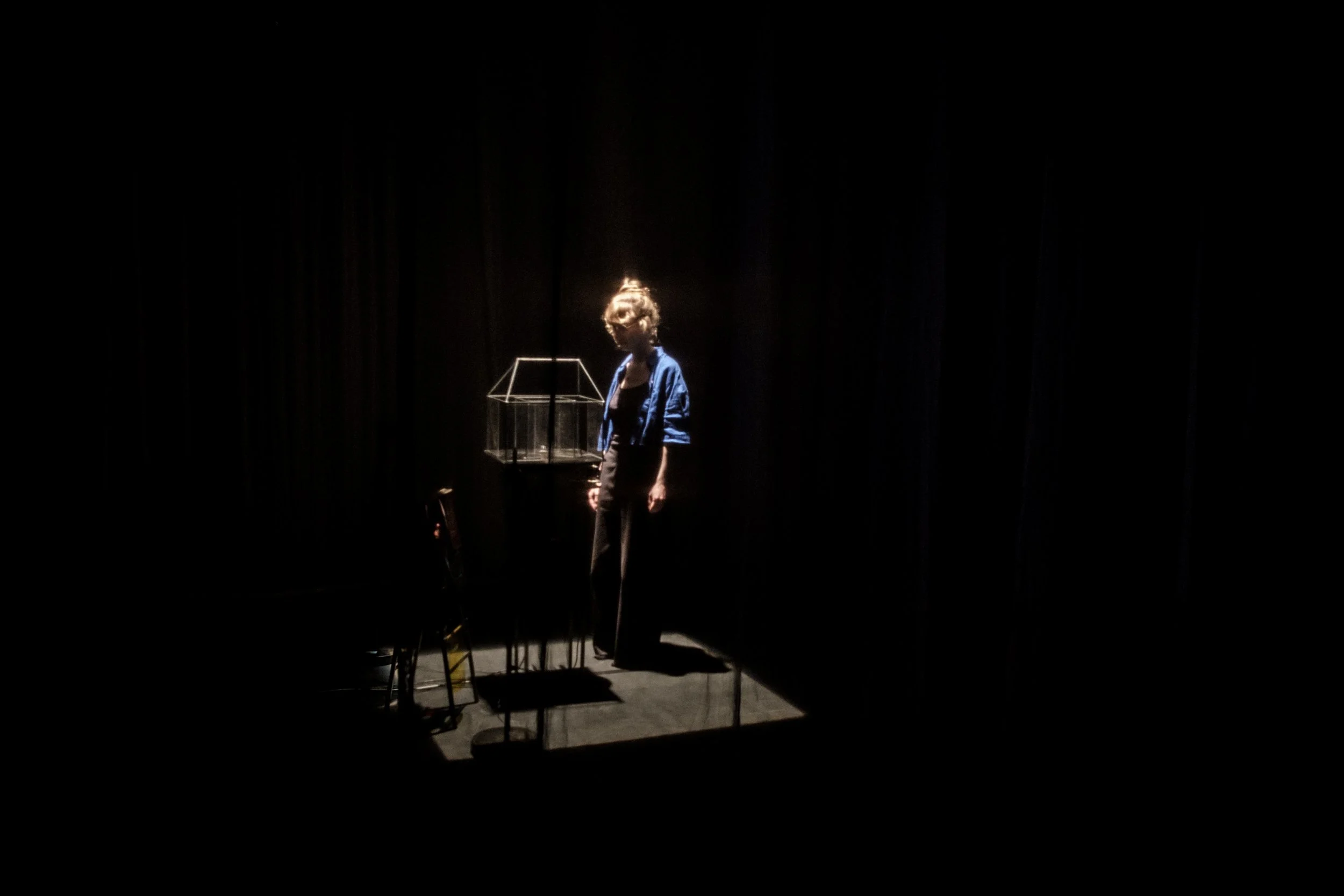 A woman standing in a dark room, illuminated by a spotlight, near a glass display case.
