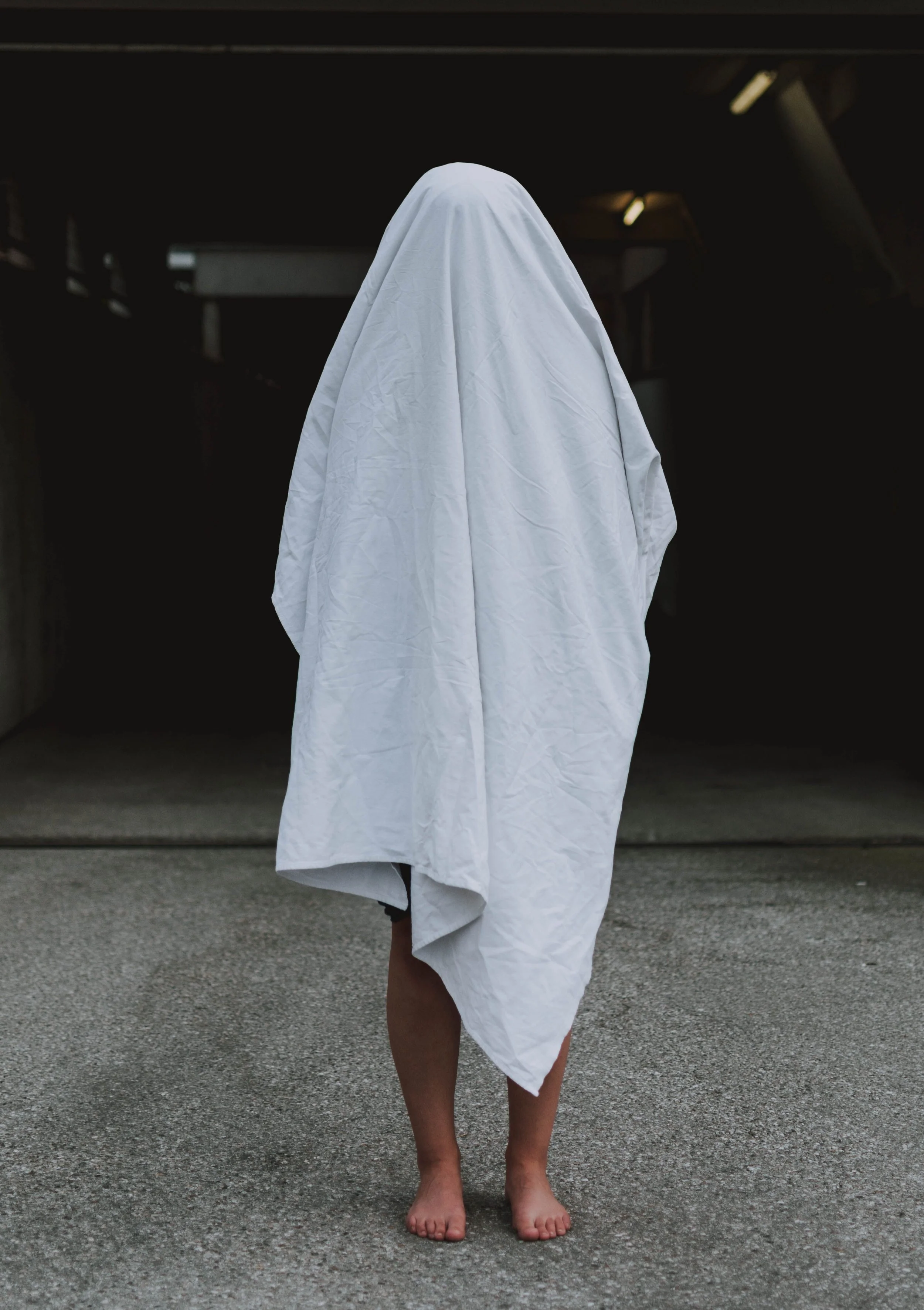 Young person standing under a large sheet, hiding