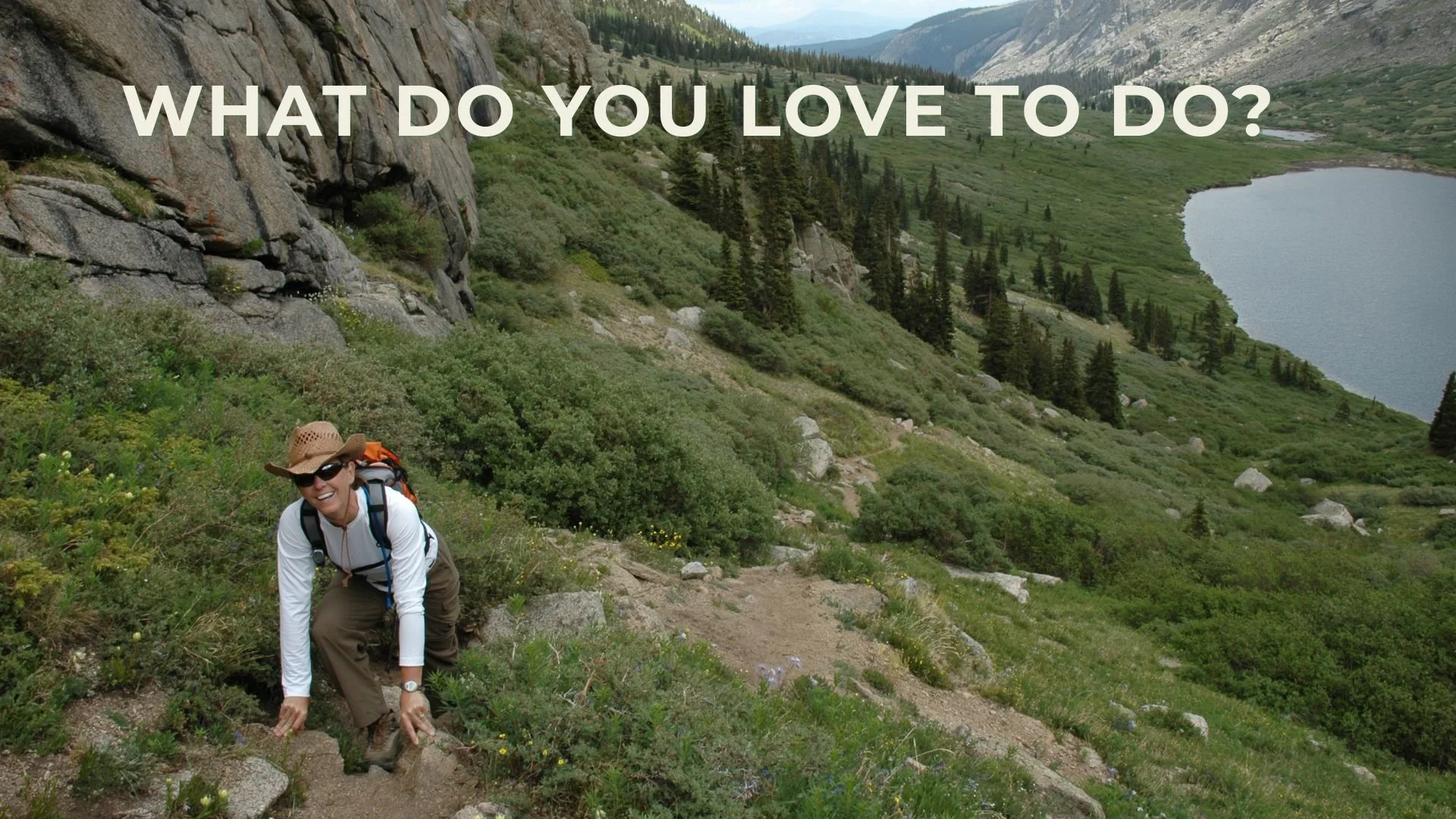 A woman hiking uphill on a trail in a green mountainous area with a lake in the background, smiling and carrying a backpack, wearing sunglasses and a hat. Question reads, "What do you love to do?"