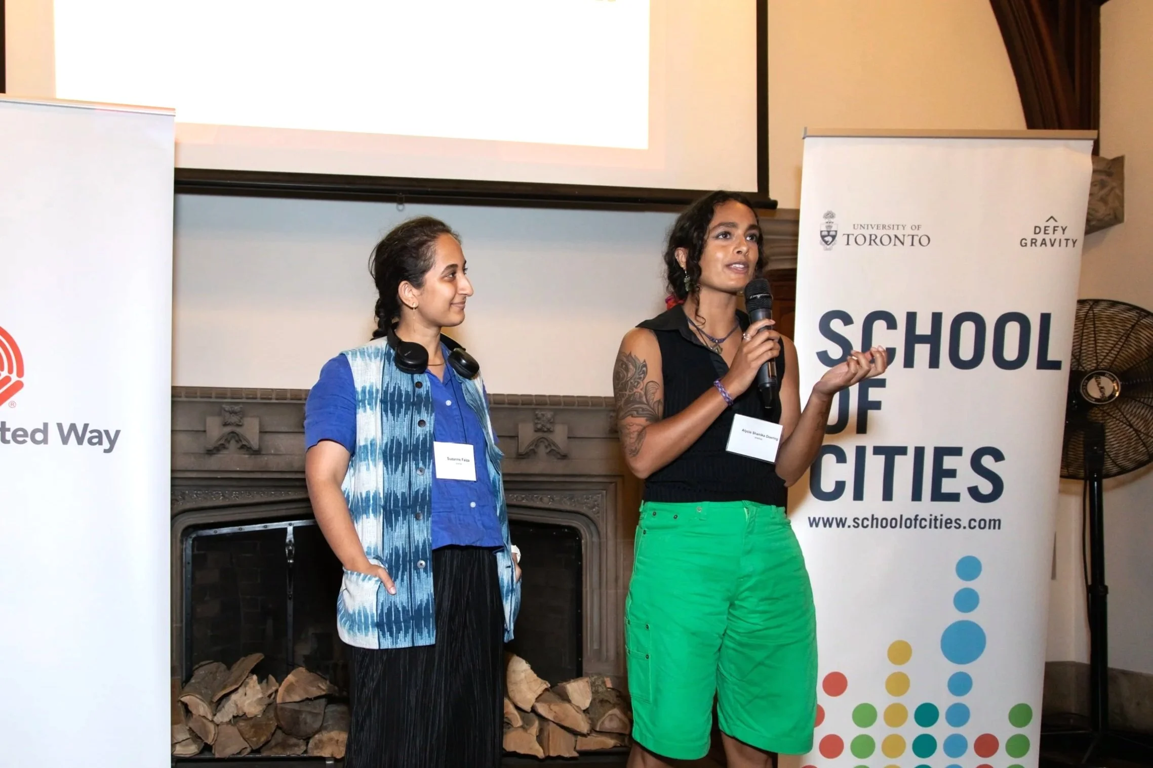 Two women speaking at a presentation, one holding a microphone, with banners behind them promoting the University of Toronto and School of Cities.