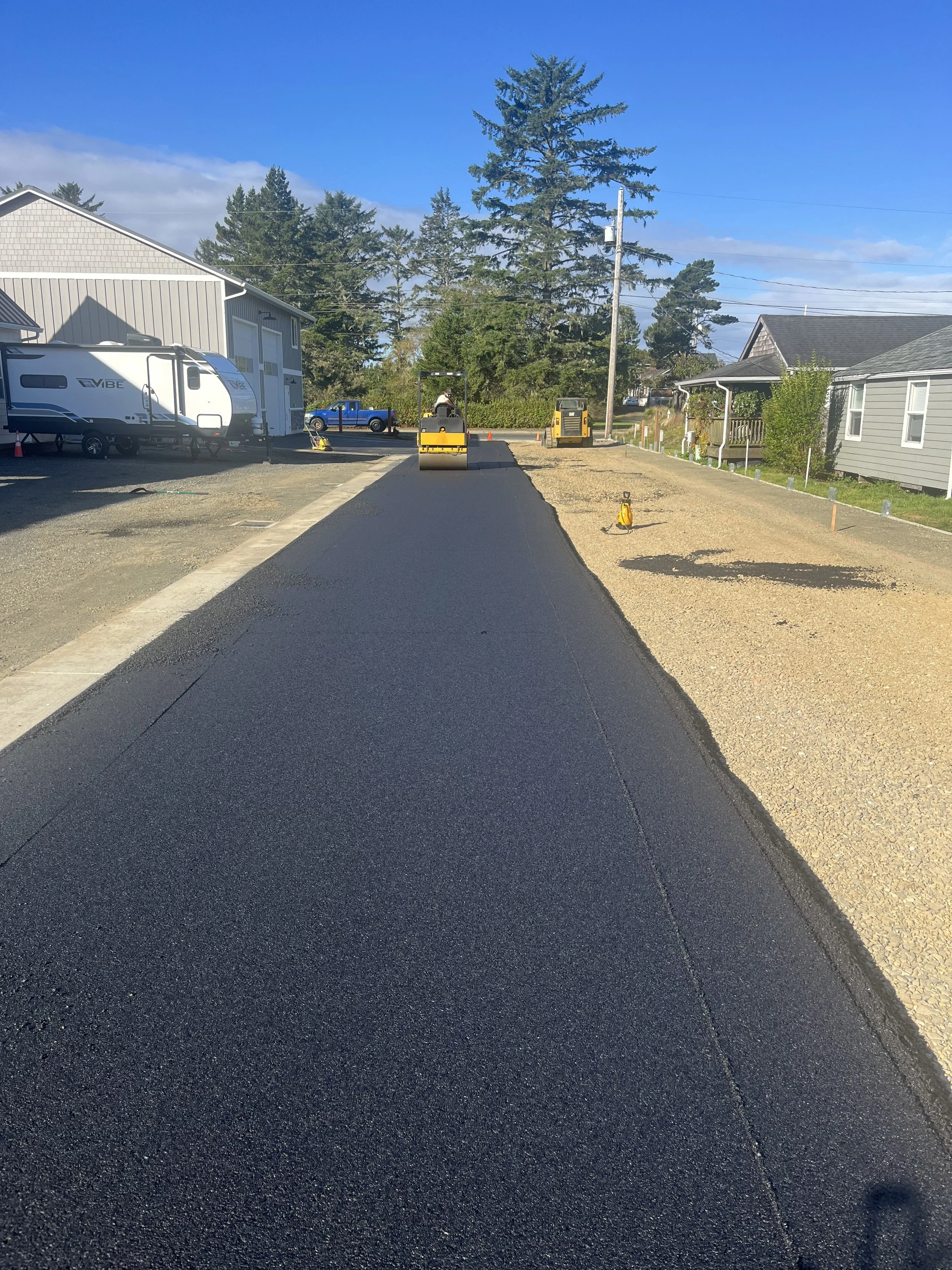 Construction workers paving a freshly asphalted road in a residential neighborhood on a sunny day.