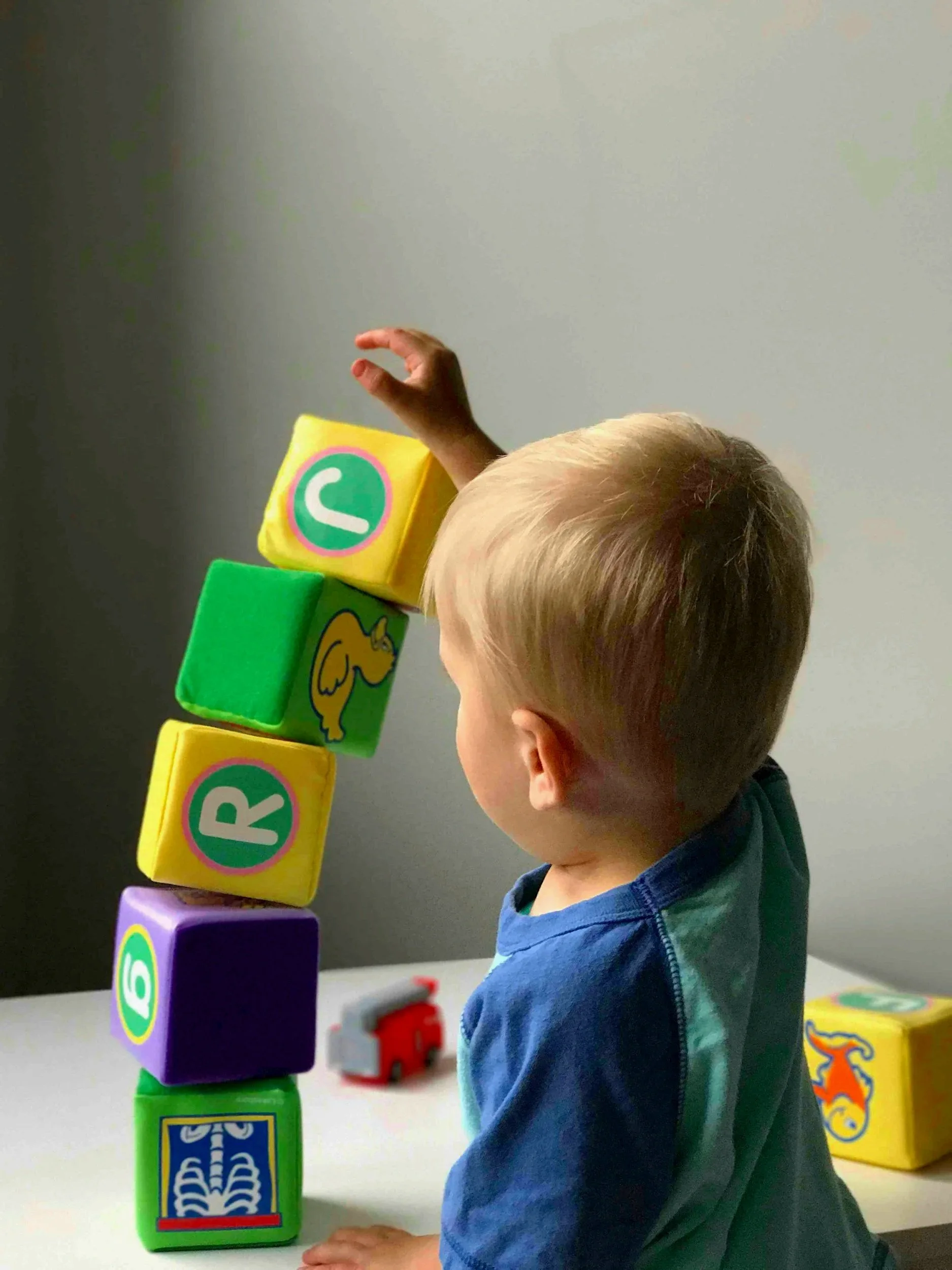 A young boy stacking colorful foam alphabet blocks on a table, with some blocks featuring animals and letters.
