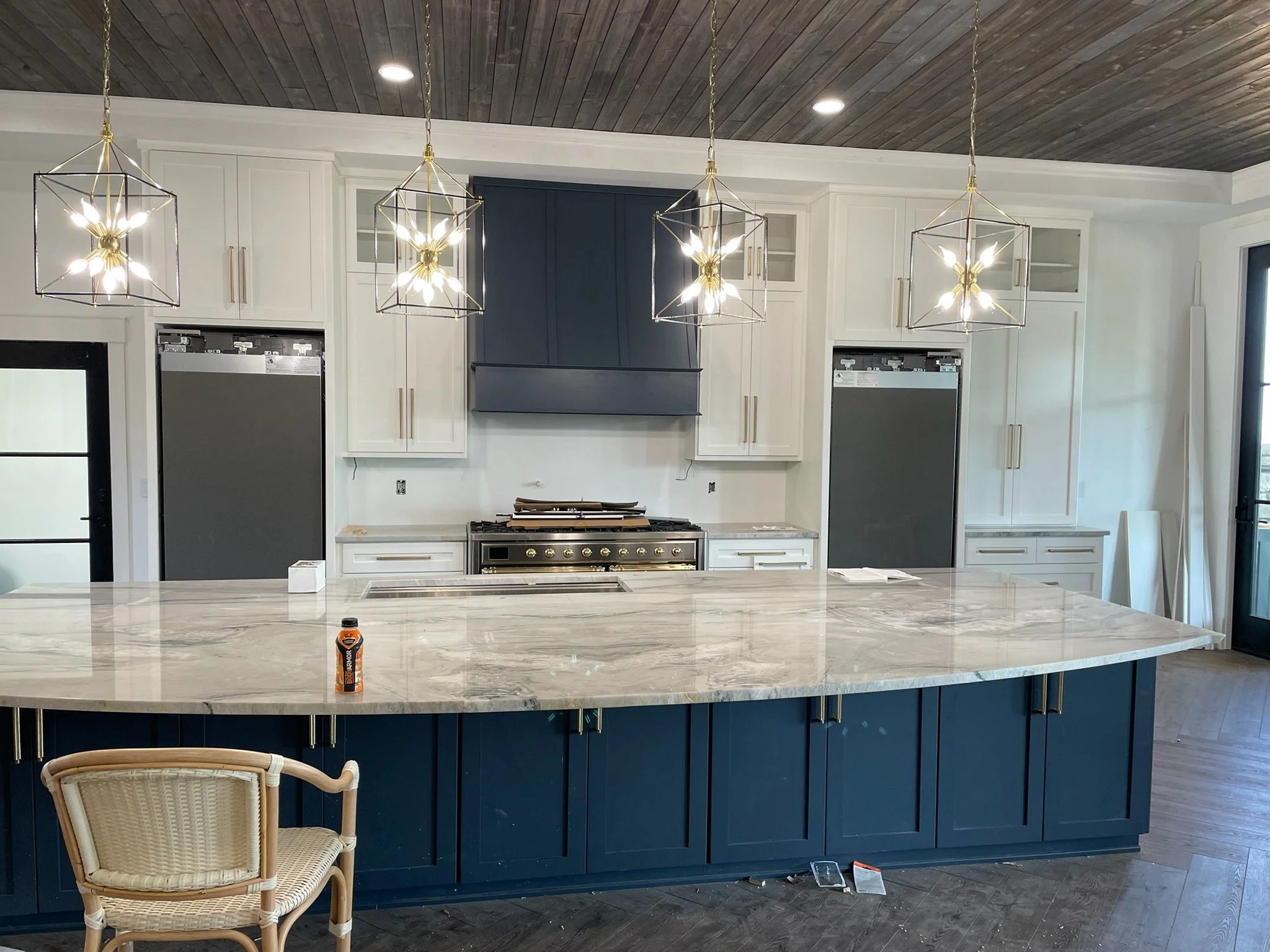 Modern kitchen with white and navy blue cabinetry, marble island, pendant lighting, and stainless steel appliances.