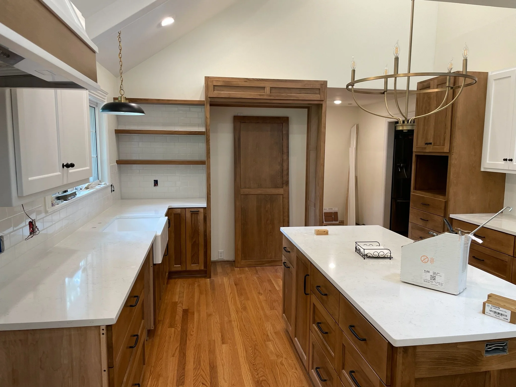 Modern kitchen with white and wood cabinets, open shelving, a central island with a white countertop, a black chandelier, and hardwood floors.