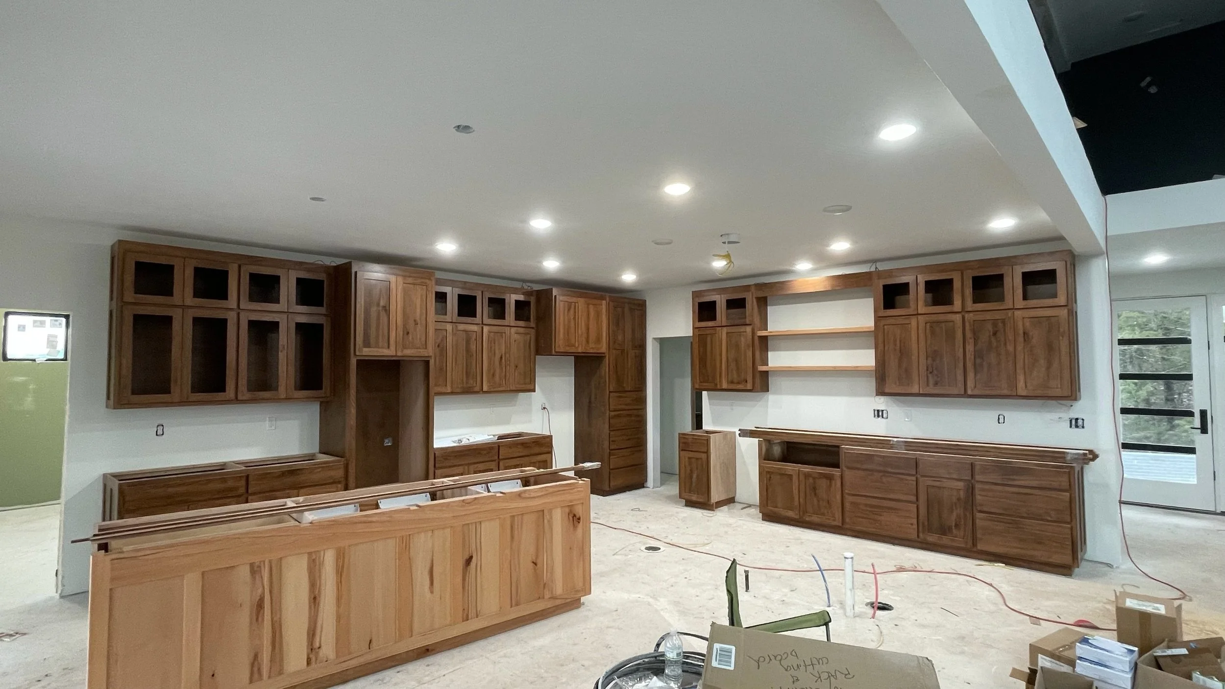 Kitchen under construction with unfinished wooden cabinets, open shelves, and construction materials on the floor.