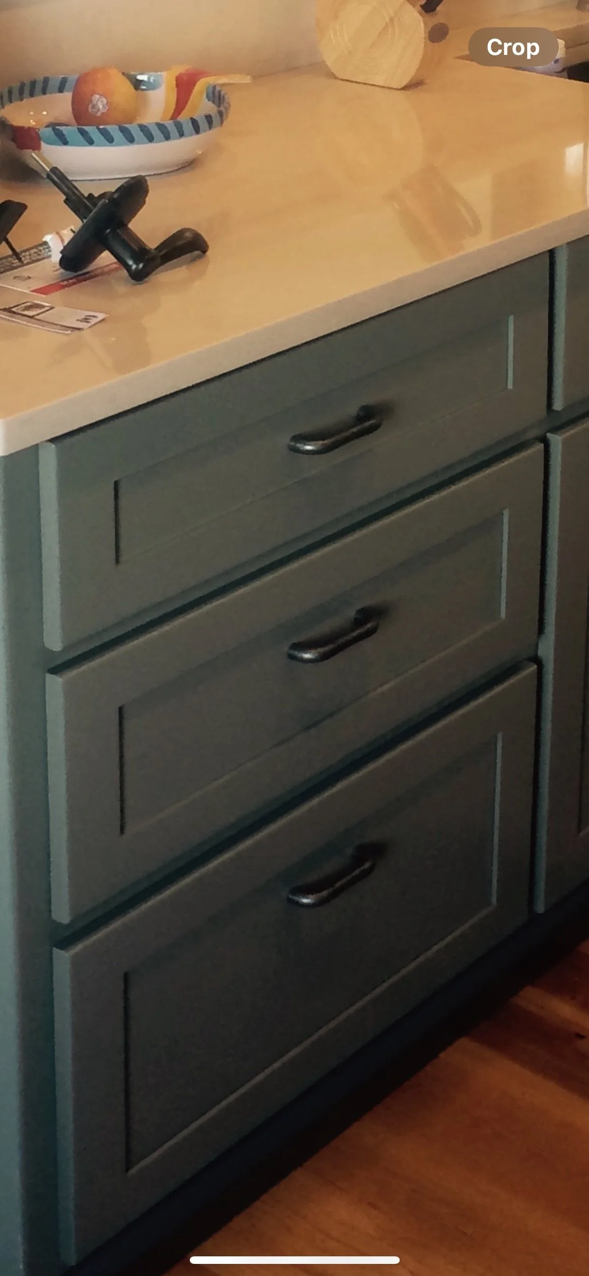 A kitchen countertop with a bowl of fruit, a black cordless phone, and some paper receipts. There are three gray drawers with black handles underneath the countertop.